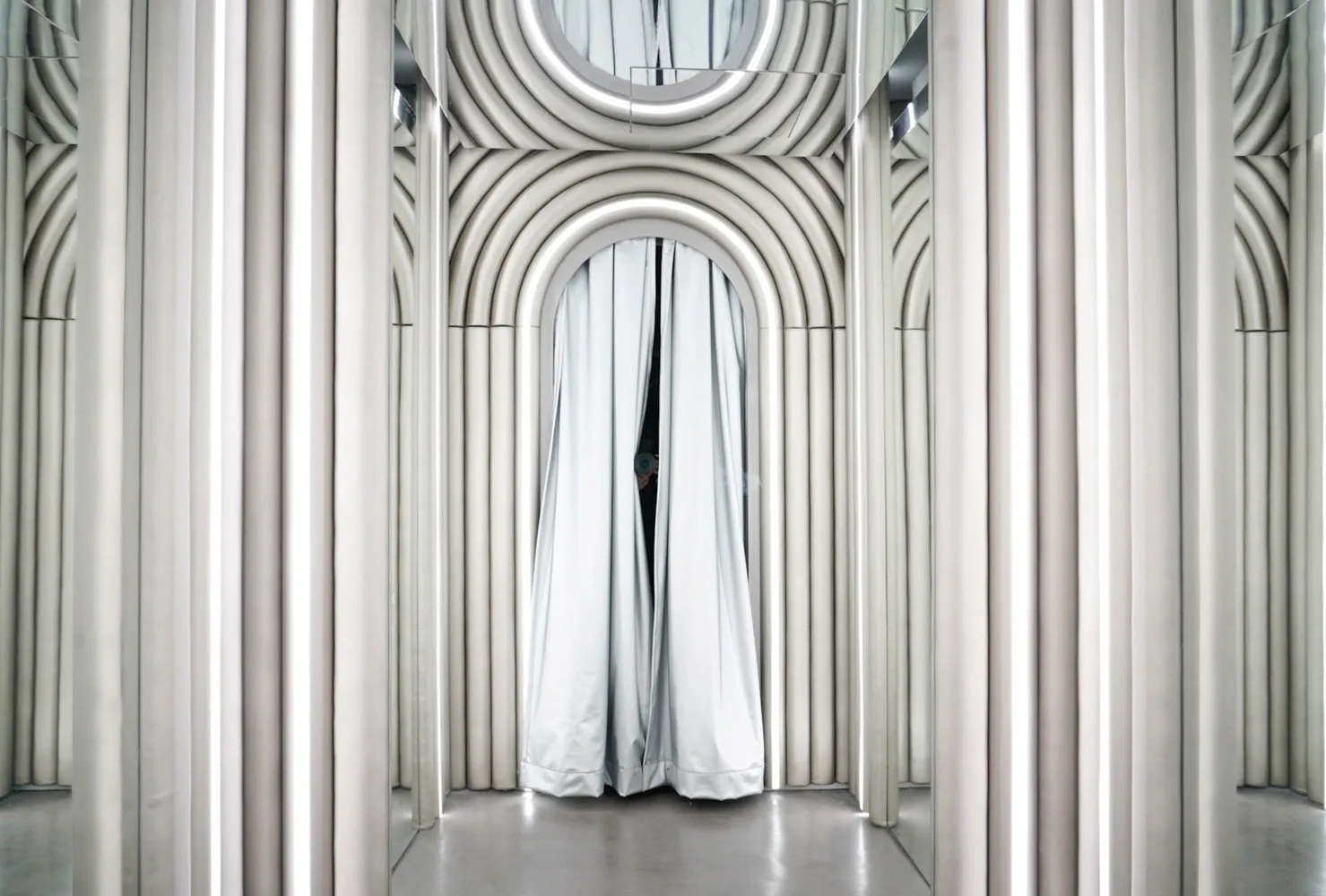 A modern interior space with a large mirrored wall reflecting a person in white clothing, creating an illusion of depth and adding a touch of elegance
