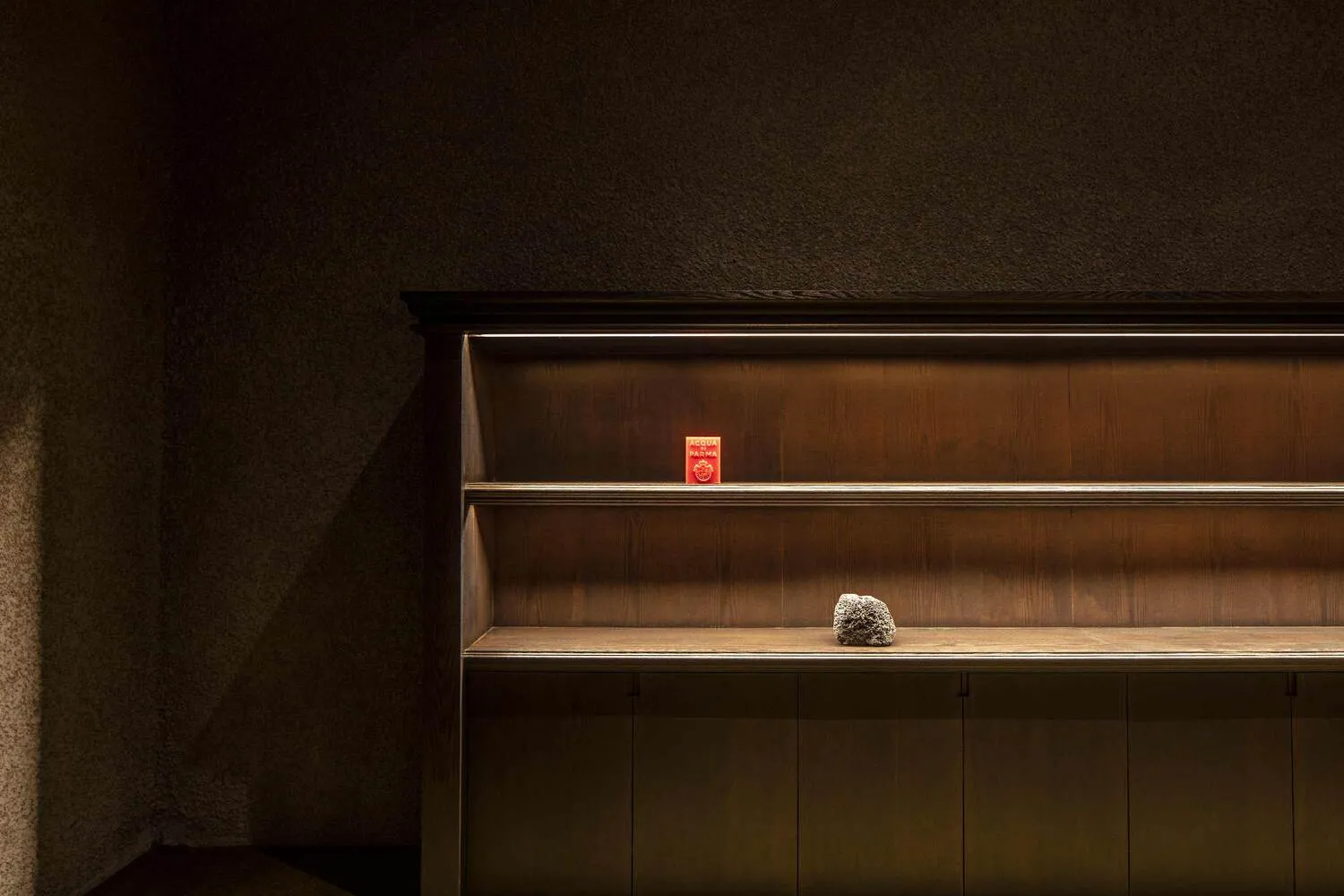 A wooden bookshelf in a darkened room with a small red object and a rock on one of the shelves