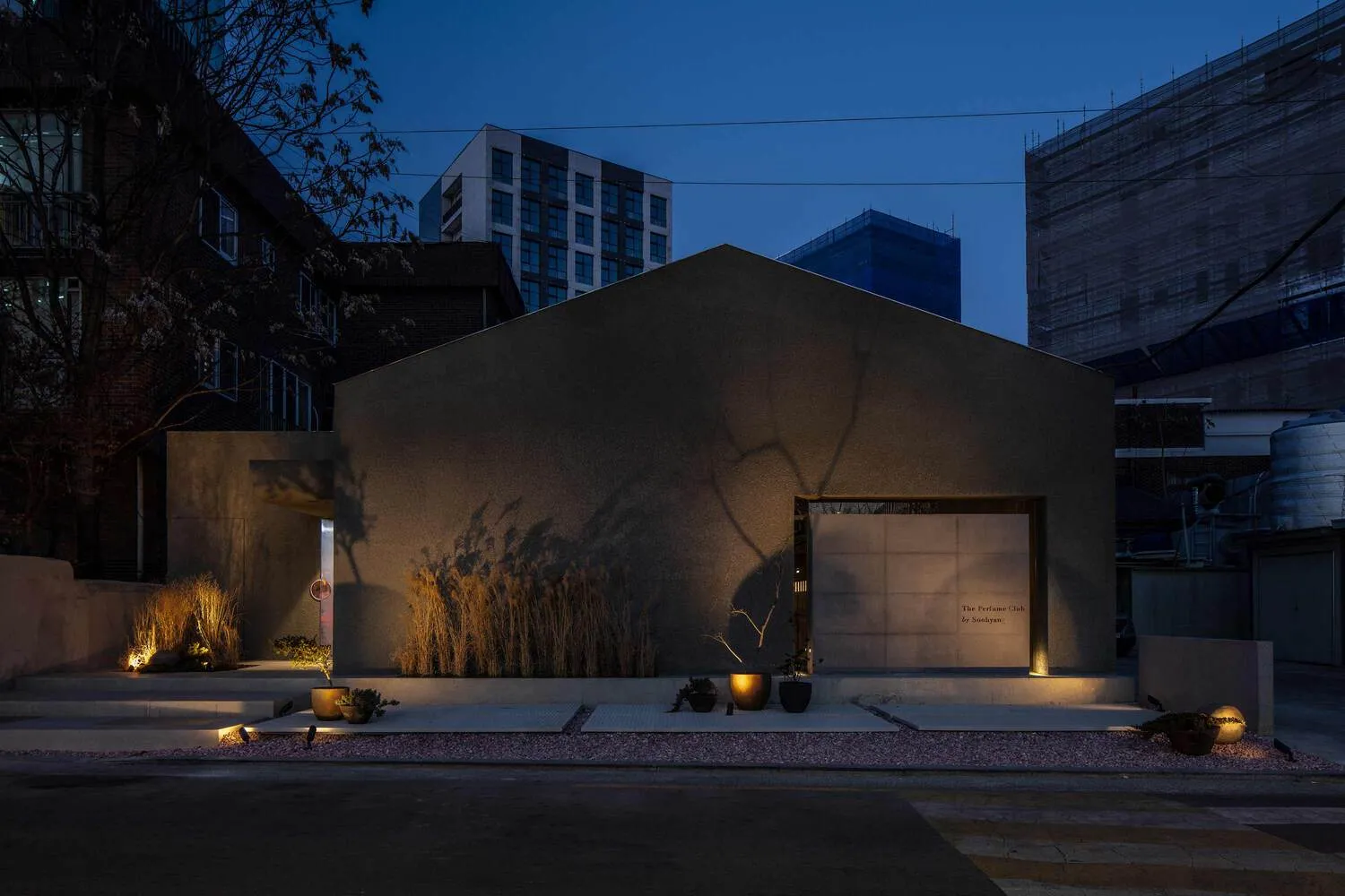 A modern building with a prominent archway and potted plants, set against a calm night sky