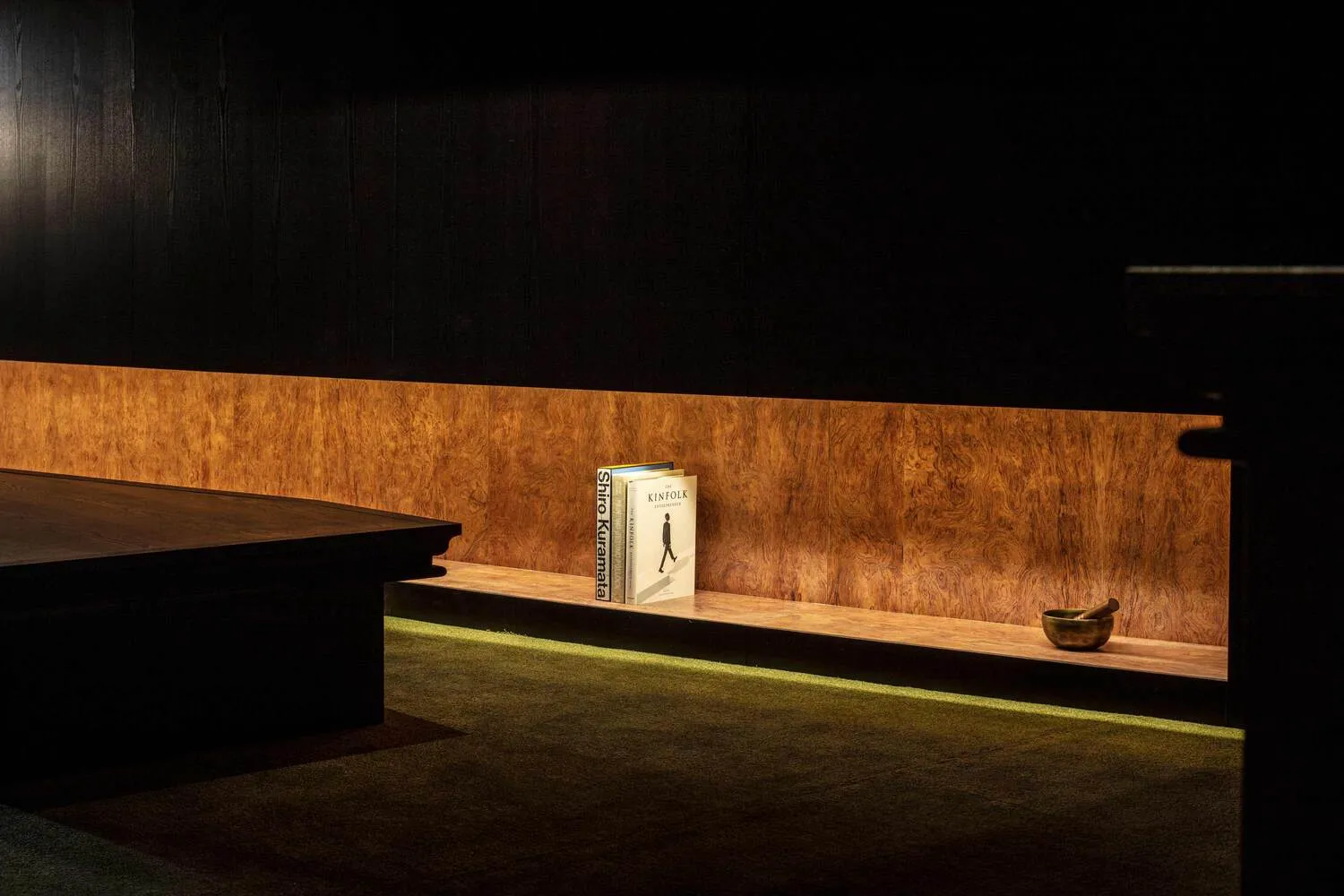 Dimly lit room with a wooden wall, a brown table, and a book and two bowls placed on it