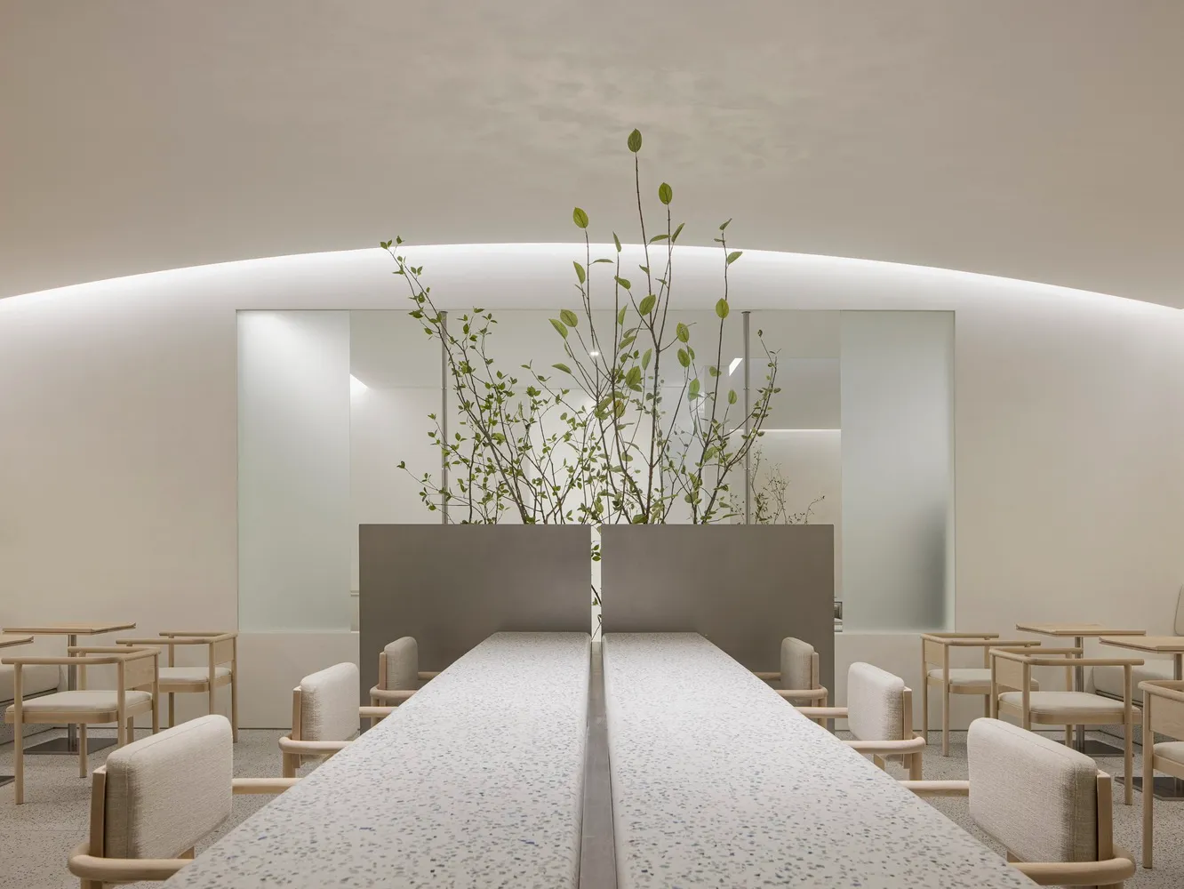 A clean and inviting restaurant interior with a long dining table, chairs, and potted plants