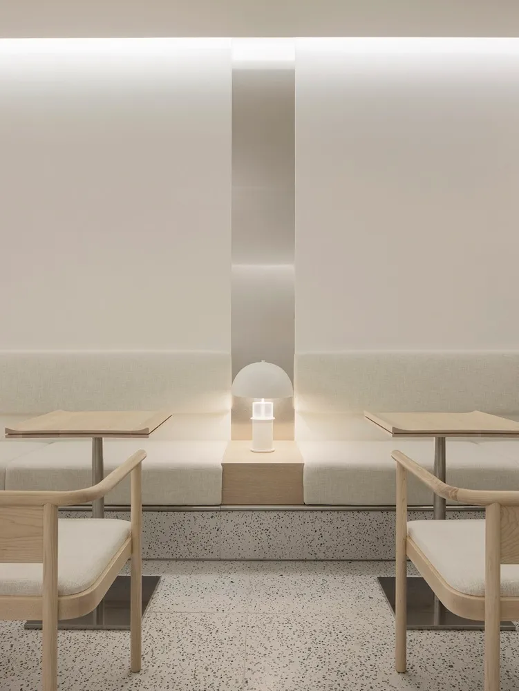 Empty minimalist room with white walls and floors, featuring three couches, two chairs, and a small lamp, creating a calm and minimalistic atmosphere