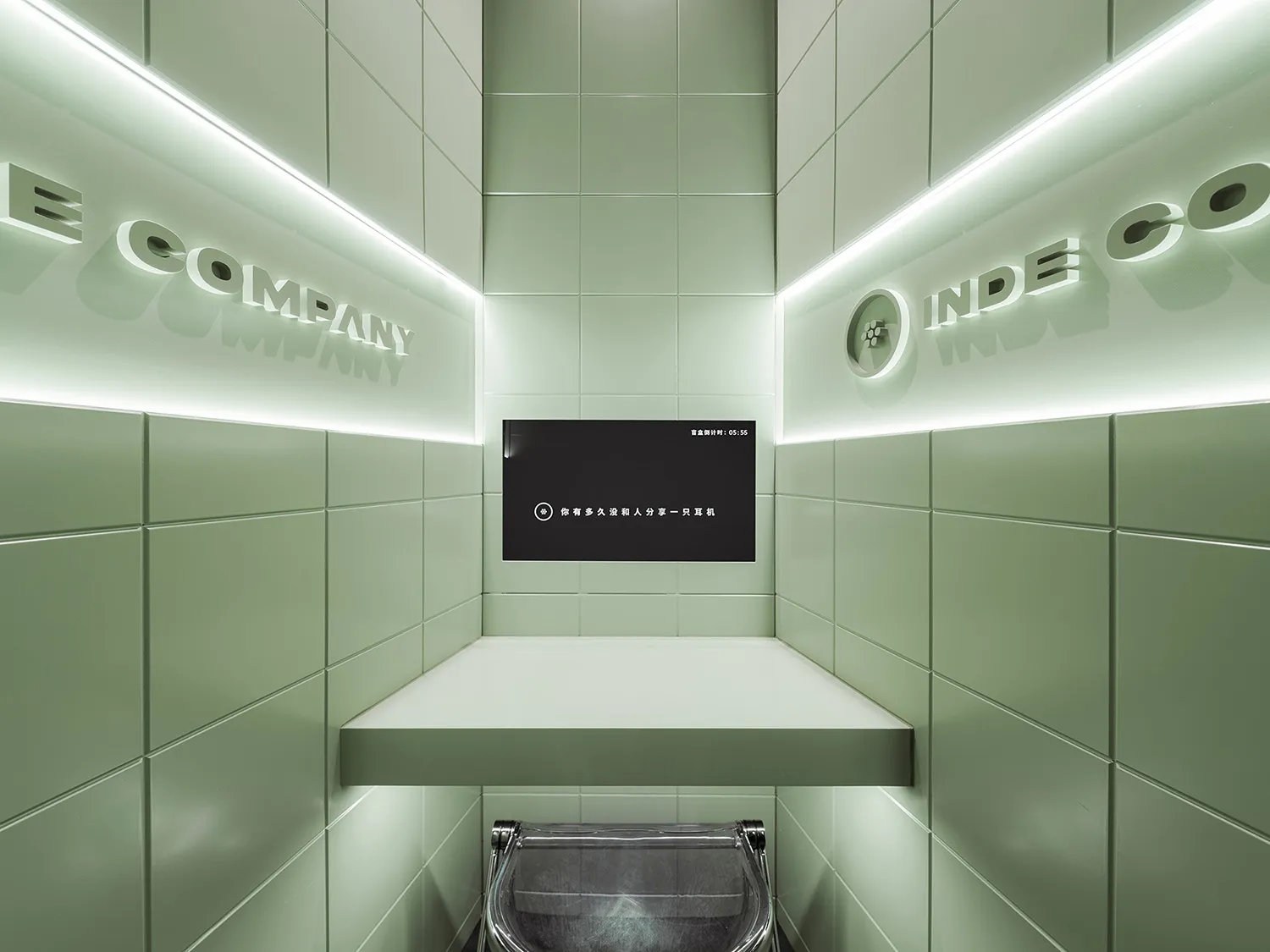 Bathroom with green tiles, two sinks, and a TV above one sink, in a well-lit space