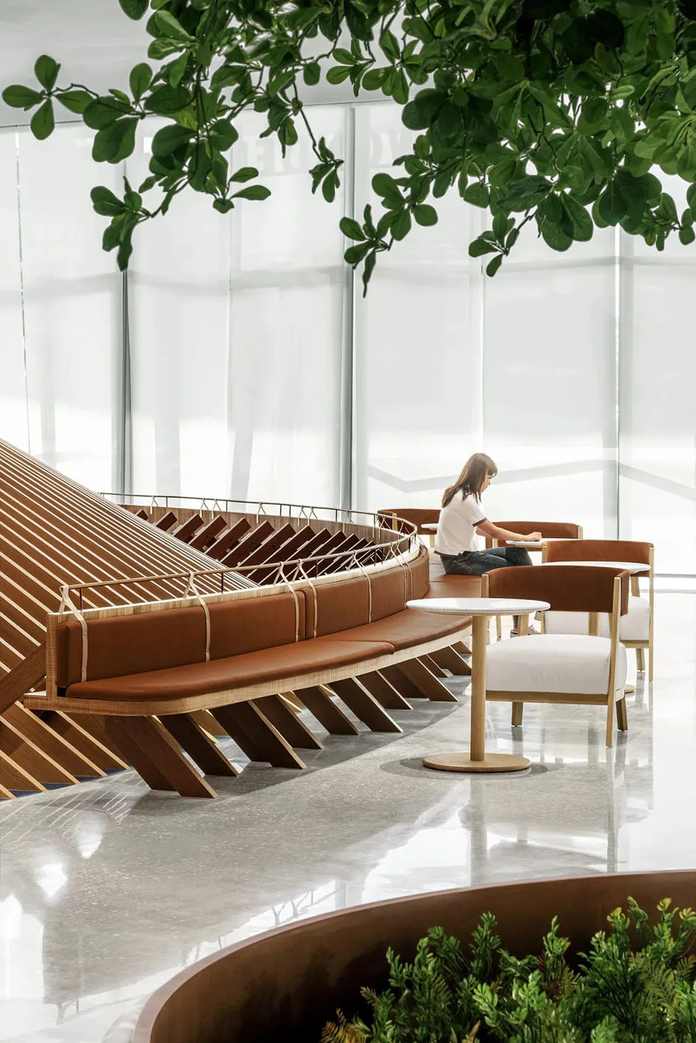 A calm and inviting indoor space with a large wooden bench and two smaller benches, featuring a woman sitting on one of them