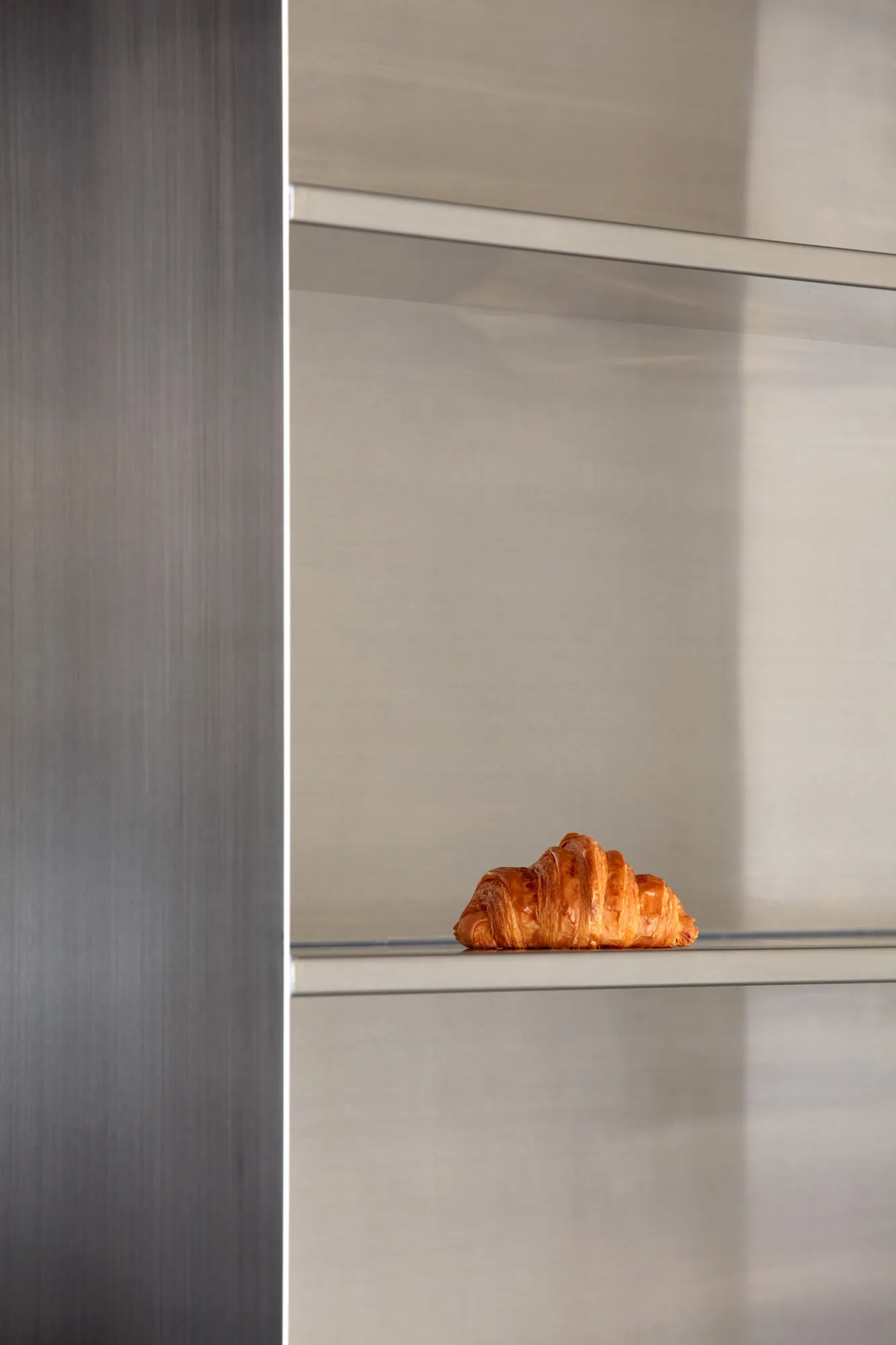 A close-up of a croissant on a silver surface in a modern kitchen with minimalist design