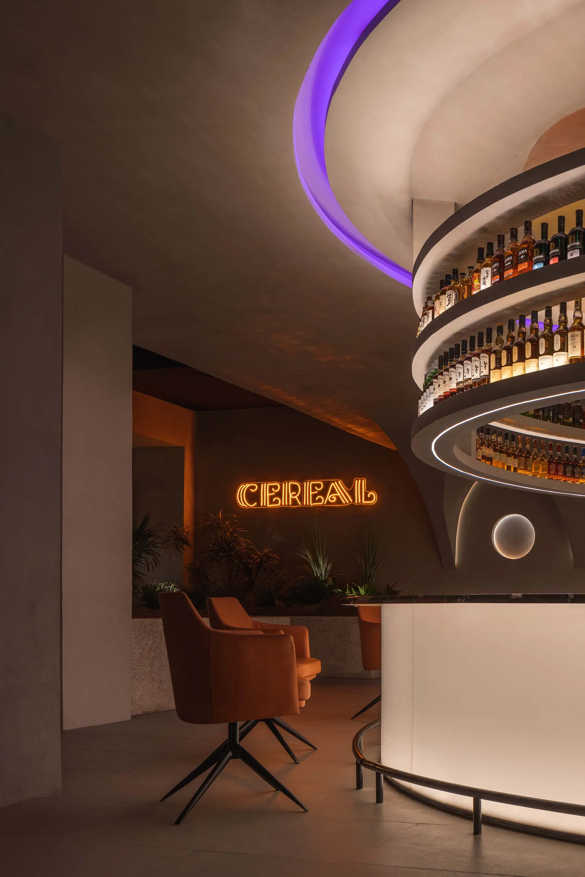 Modern bar with a spiral design, liquor bottles on the walls, and seating for patrons