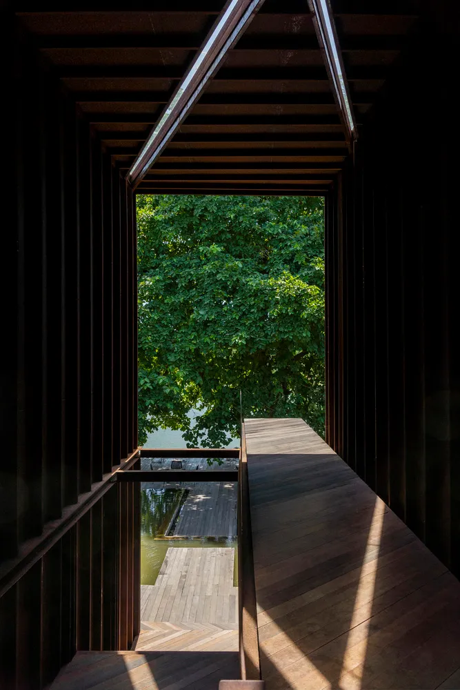 A waterfront building with a wooden deck and large windows, surrounded by natural scenery