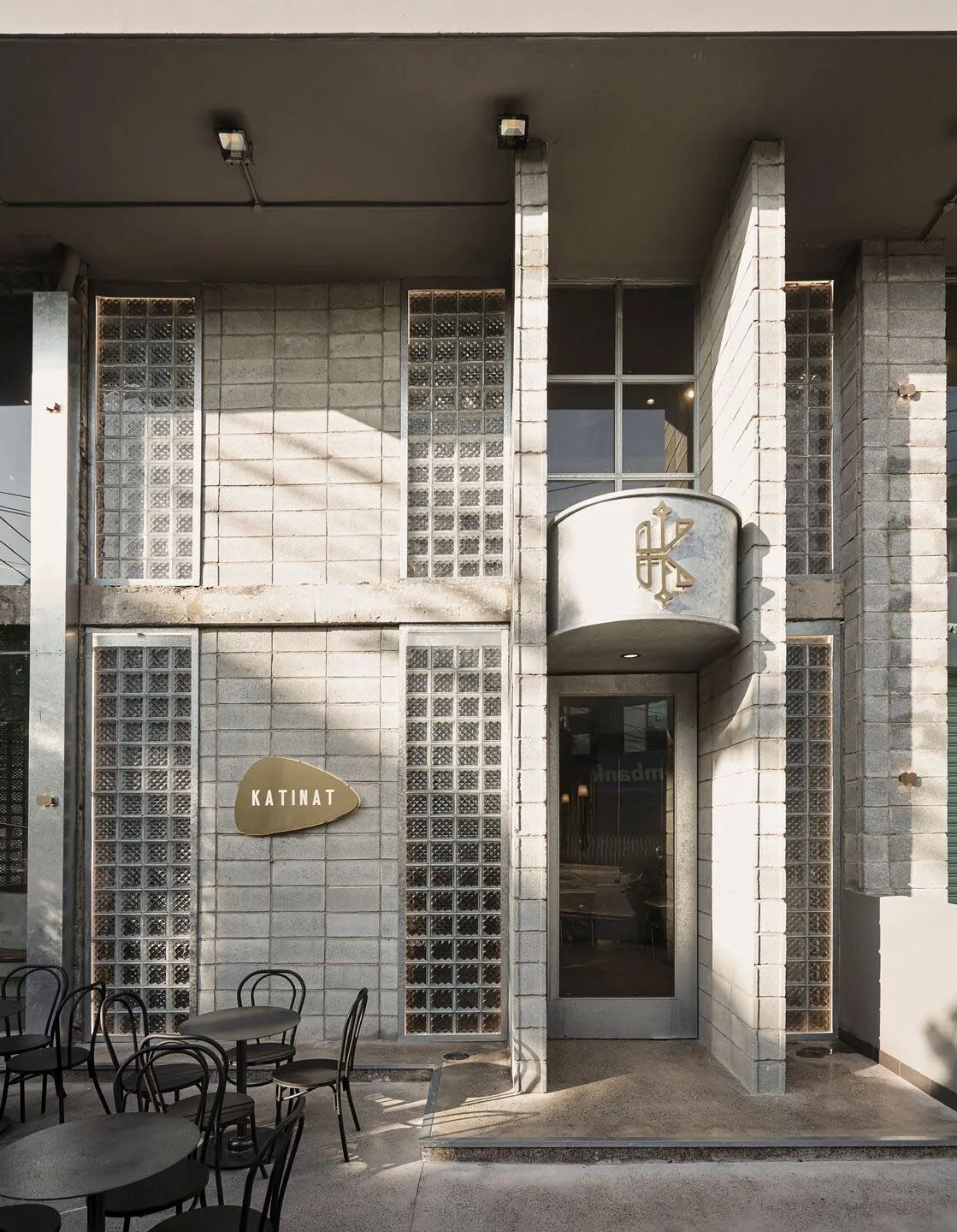 A modern building exterior with a large glass wall and a patio area featuring various-sized chairs in different positions, inviting a comfortable outdoor seating experience