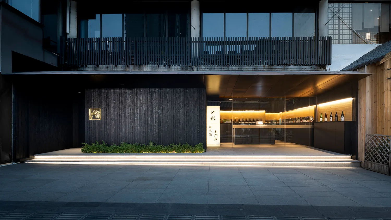 Contemporary Asian restaurant with a black facade, glass front door, and a spacious interior featuring a bar area with wine bottles and potted plants