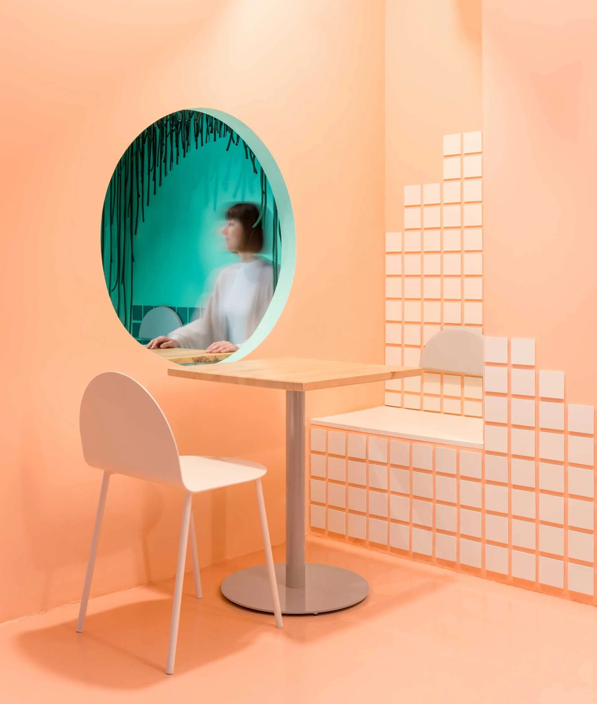 A woman sits at a dining table in front of a mirror, surrounded by white furniture and minimalistic decorations, creating a warm and inviting atmosphere