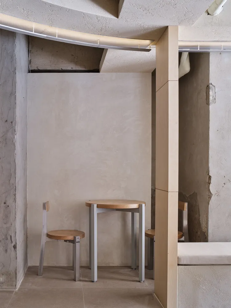 Dining area with concrete walls, a small table, and three chairs, accompanied by a bench in a modern and industrial space