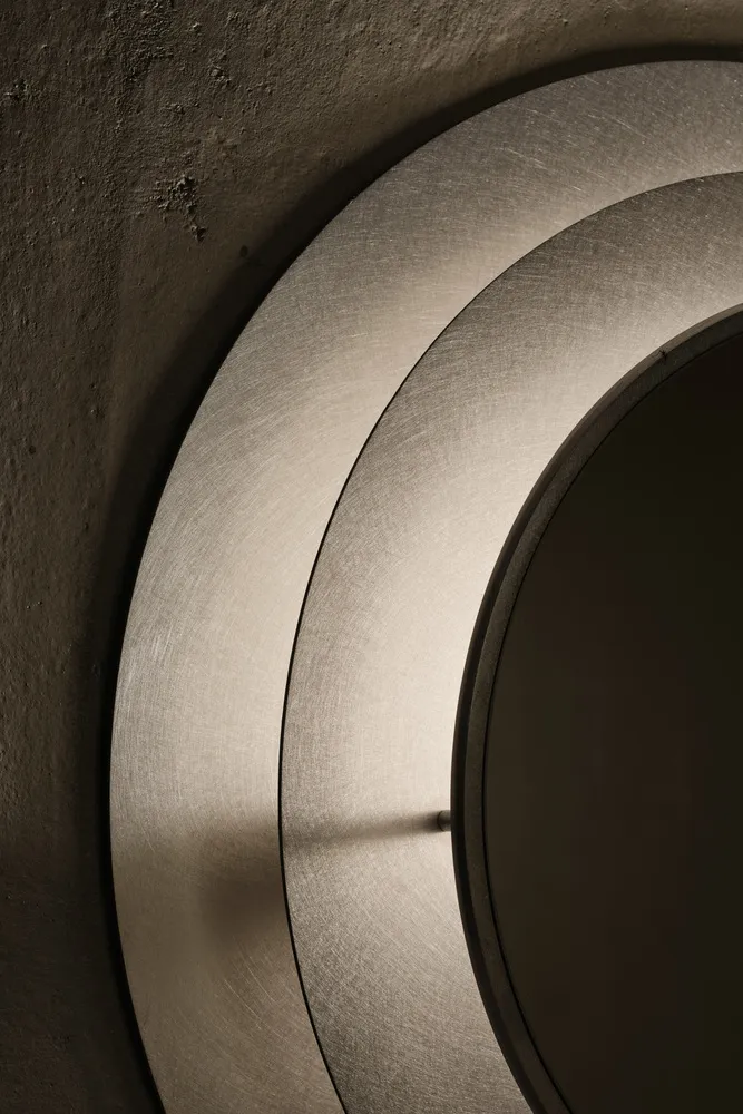 A bathroom with a round mirror on the wall reflecting a decorative piece, in a clean and well-organized space