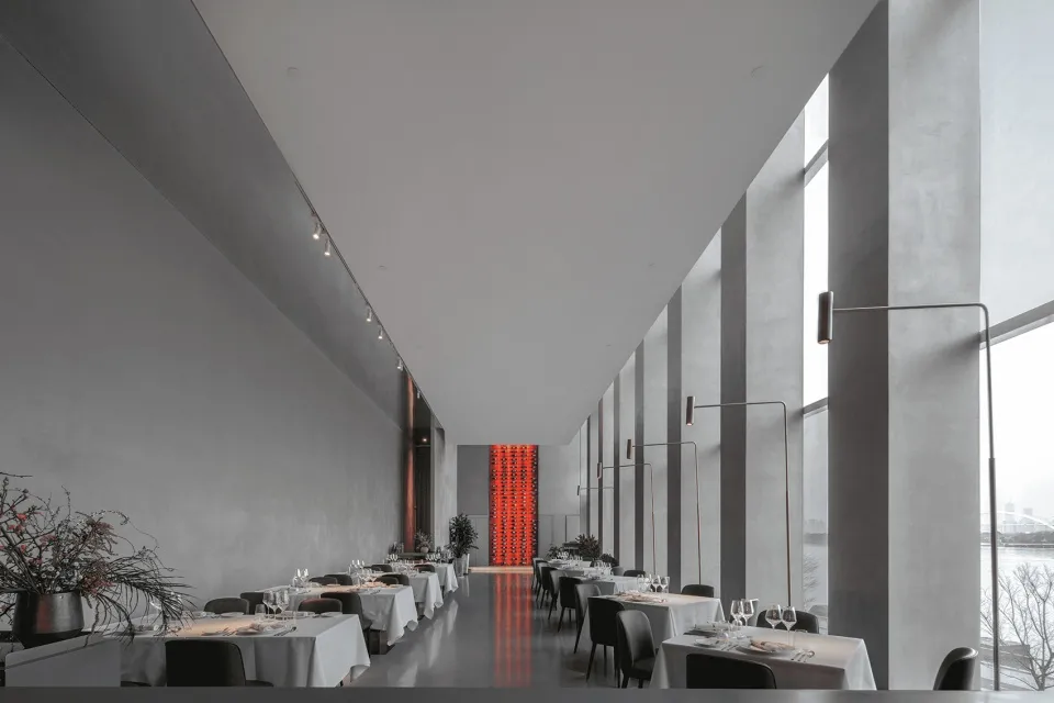 燈光柔和的餐廳內部，紅色點綴、盆栽植物，以及多張桌椅