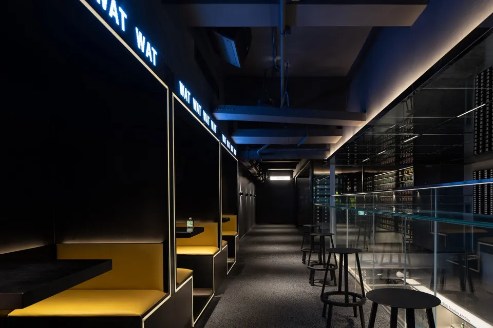 A modern restaurant or bar area with a long hallway featuring benches and chairs, overhead lighting, and a welcoming atmosphere