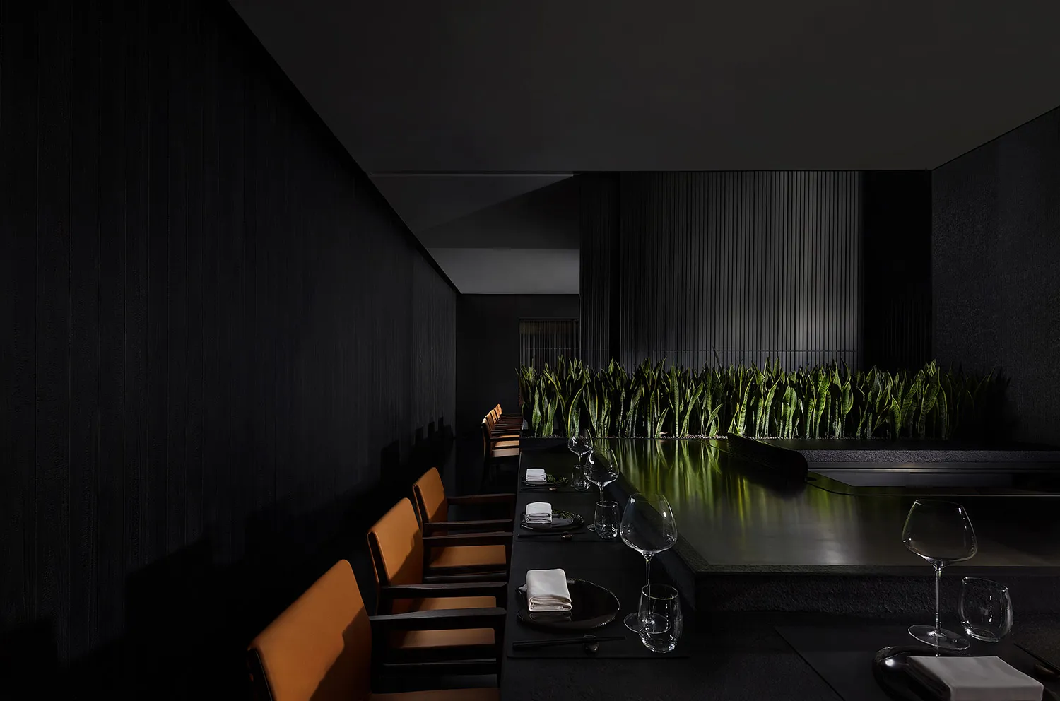 A modern dining area with a long black table and several chairs, set up for a meal, in a sophisticated atmosphere