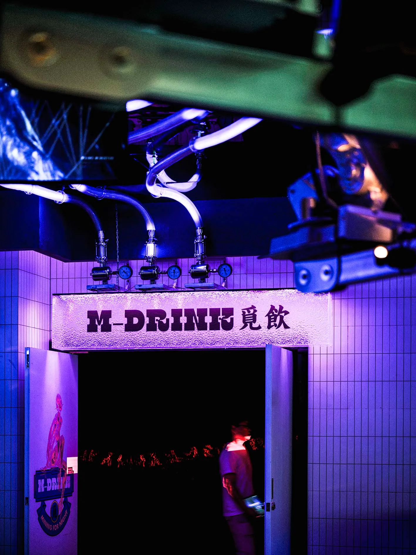 A lively Asian bar with purple lights, patrons standing near the entrance and scattered throughout the space