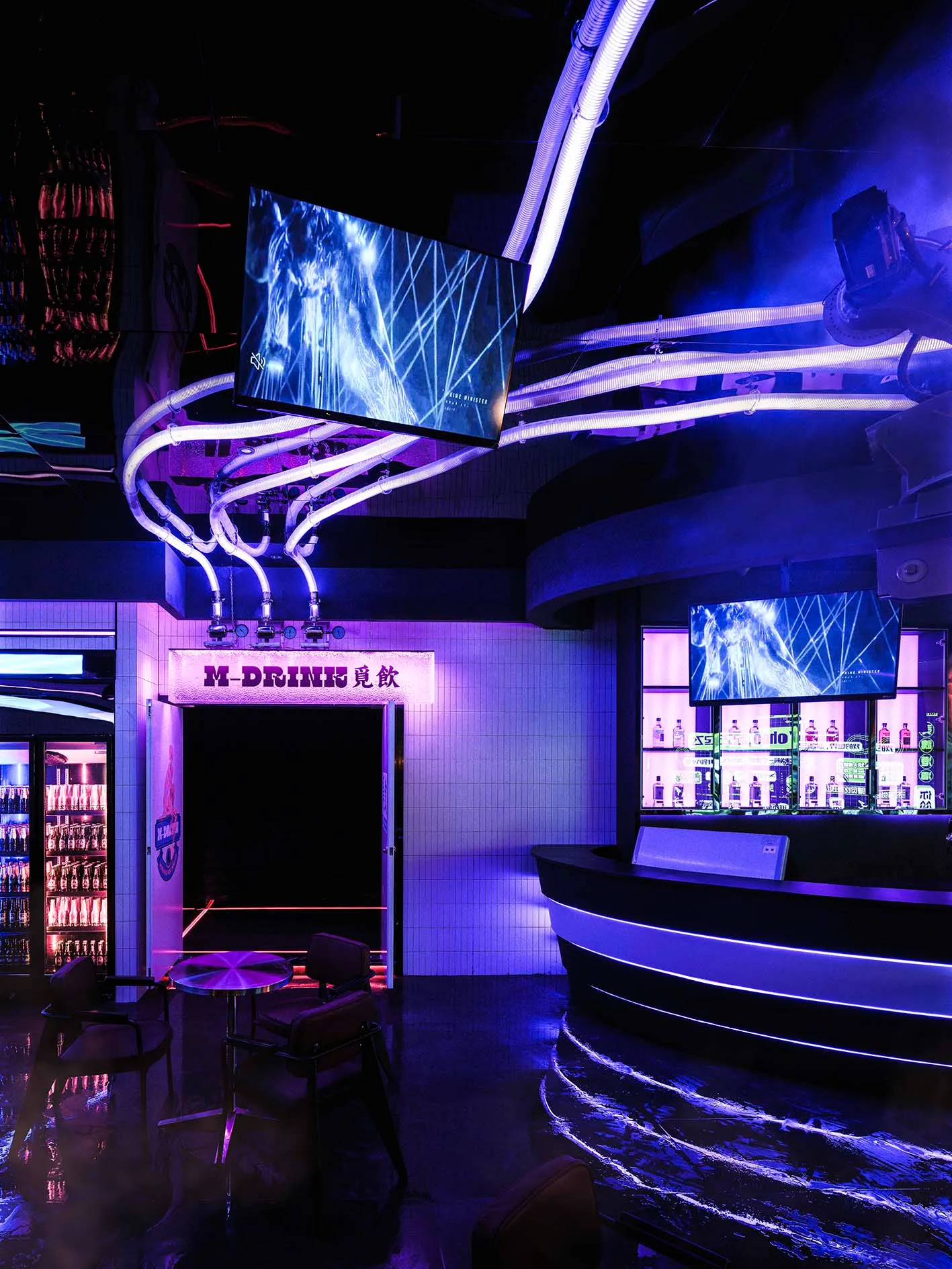 A stylish bar area with purple lighting, multiple TV screens, and comfortable seating for patrons