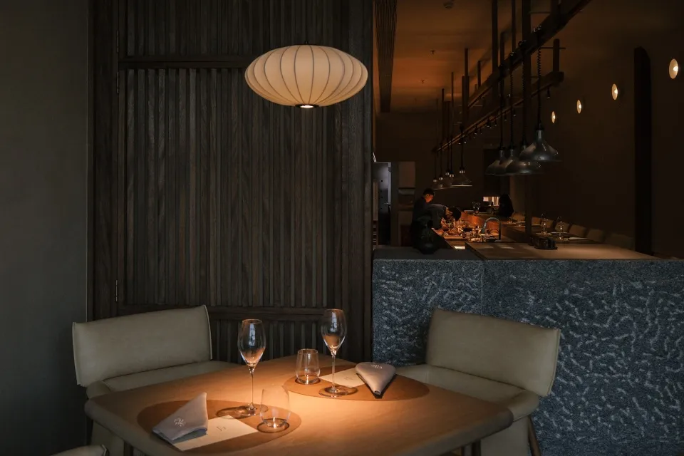 Elegant dining space with wooden tables, wine glasses, and a vase centerpiece, set in a well-lit environment