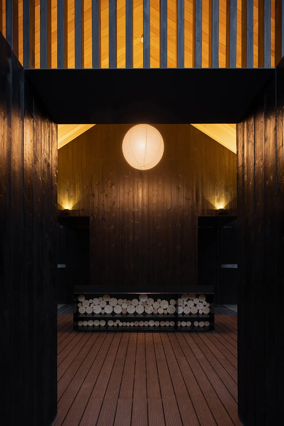 A warm and cozy living dining space with wooden walls, a central bench, and a round light fixture