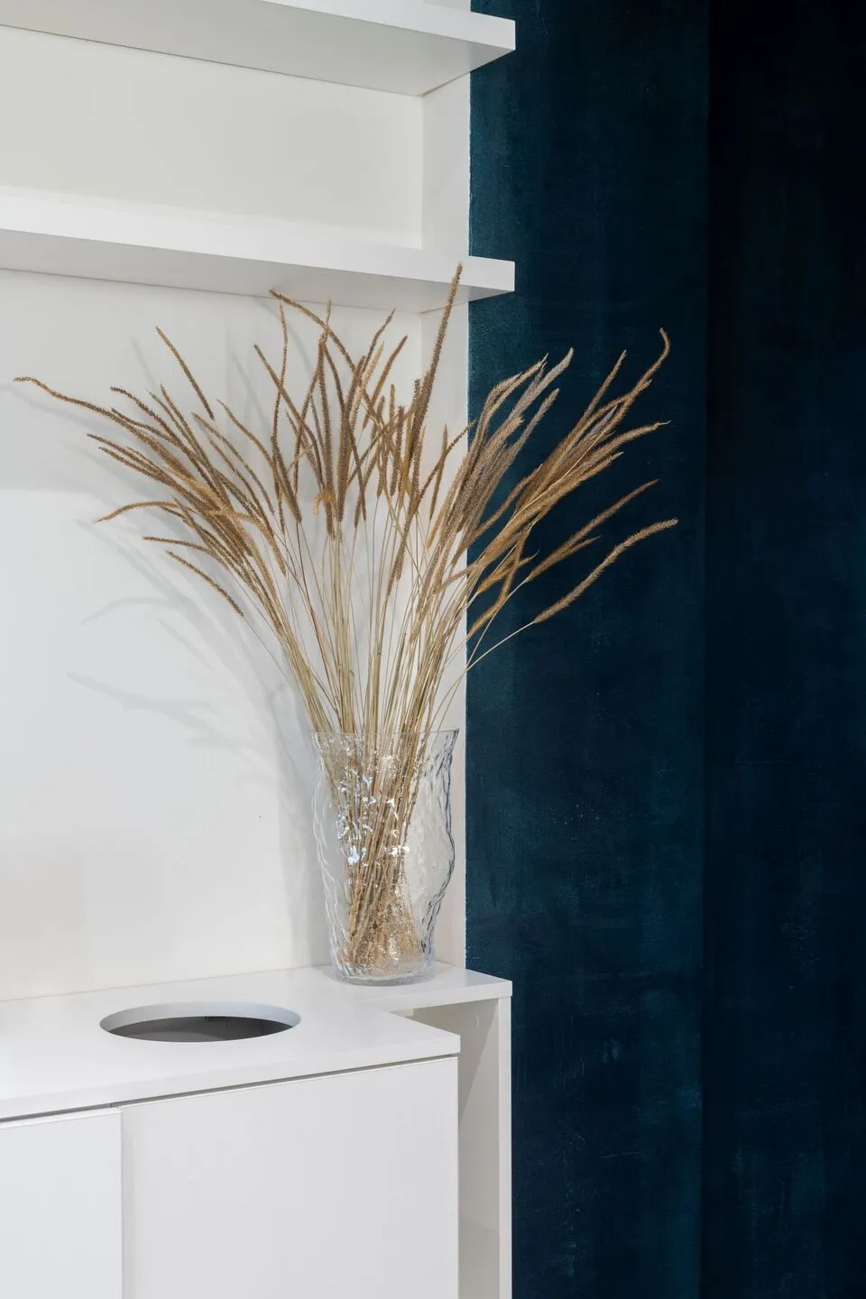 A calm and serene indoor space with a white wall, a glass vase, and dried grass as a decorative element