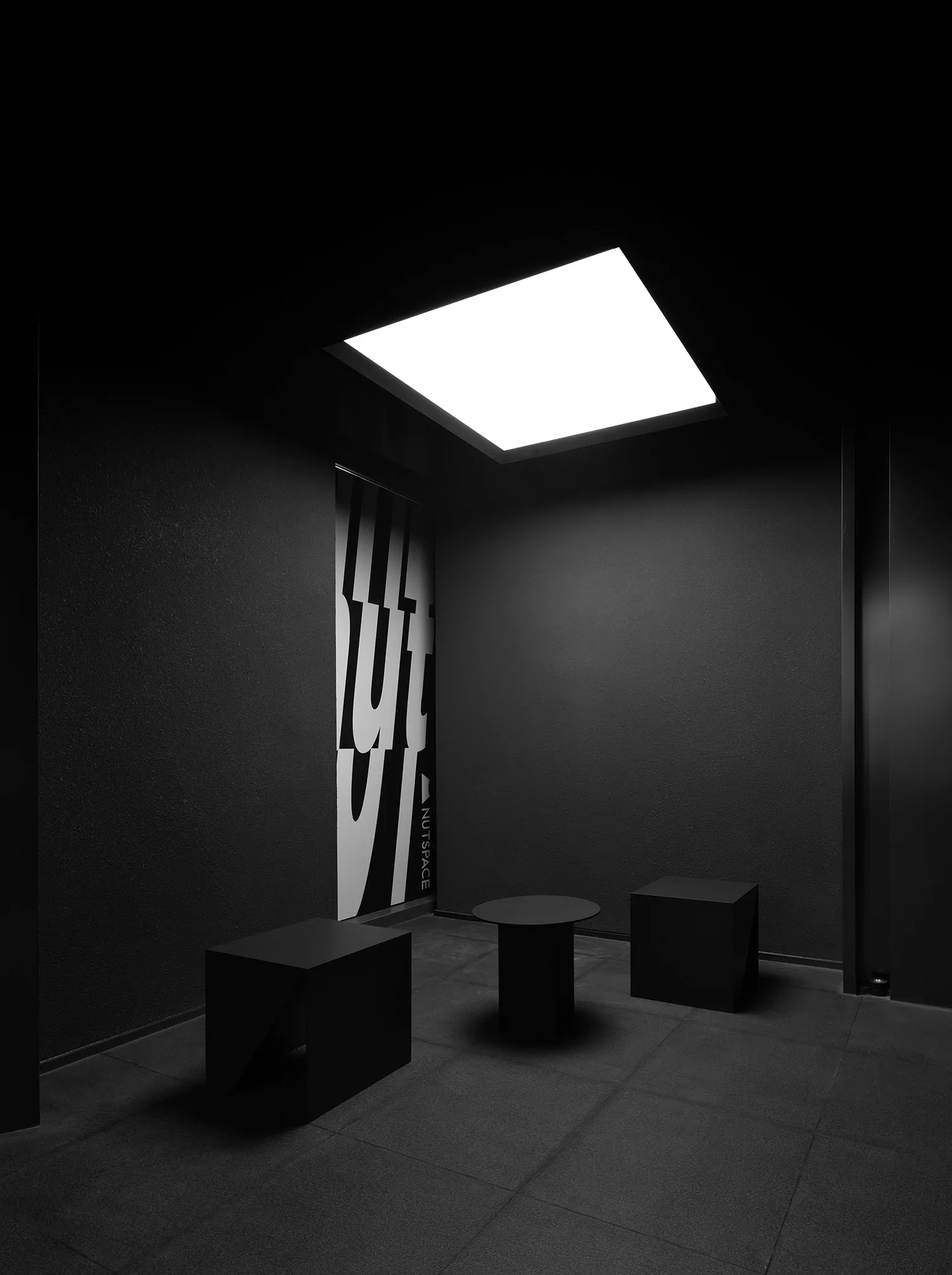 Dark modern room with three small tables and concrete walls, lacking natural or artificial light
