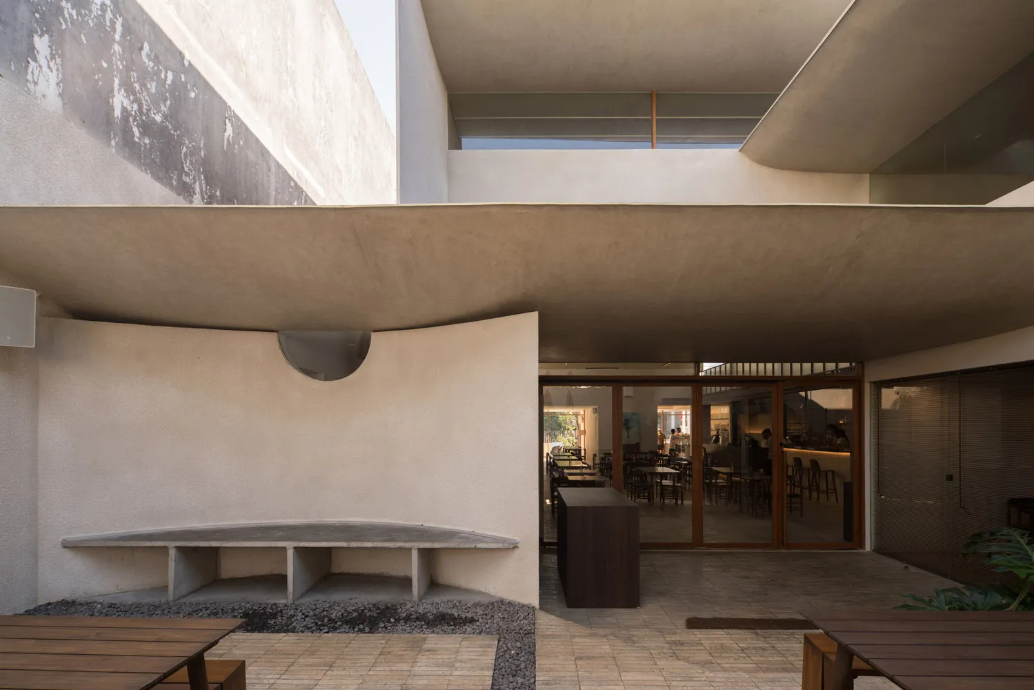 Open modern restaurant with concrete walls, wooden tables, and pendant lighting