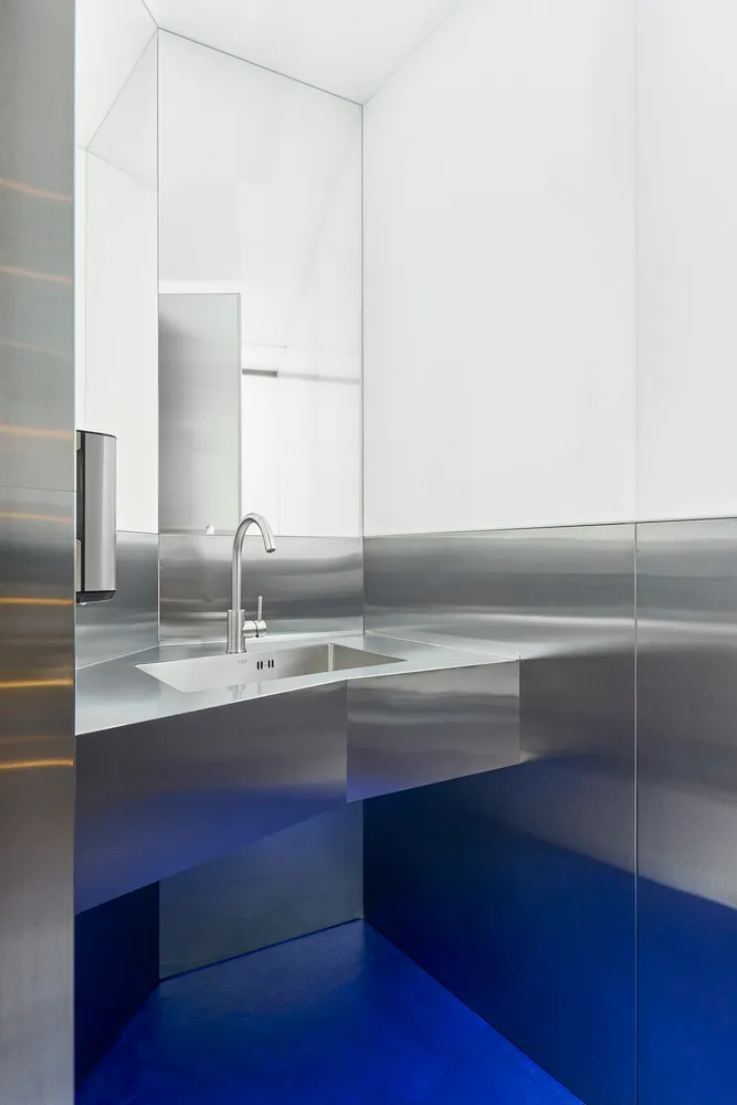 Industrial bathroom with a metal sink and mirror, featuring a silver-framed mirror and a well-lit atmosphere