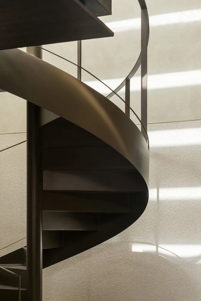 A modern metal staircase near a window, illuminated by natural light, with a sense of depth and complexity within the structure