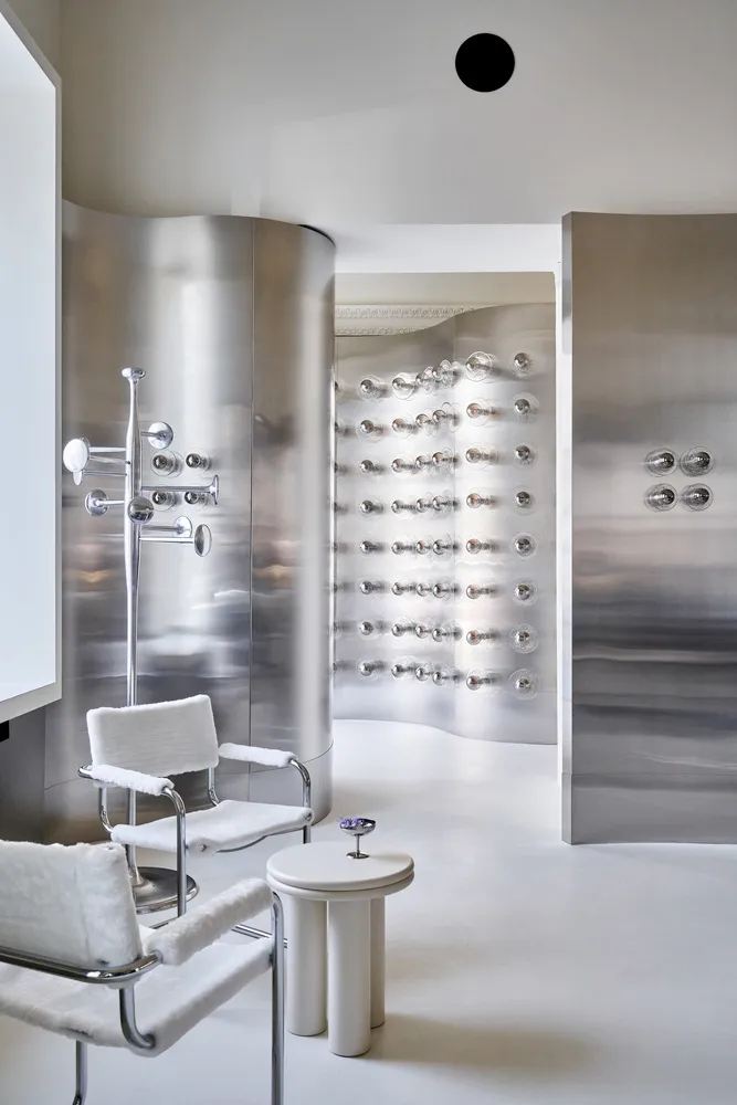 Modern interior design showroom with metal walls and floors, featuring a dining table and two chairs in a clean and minimalistic space