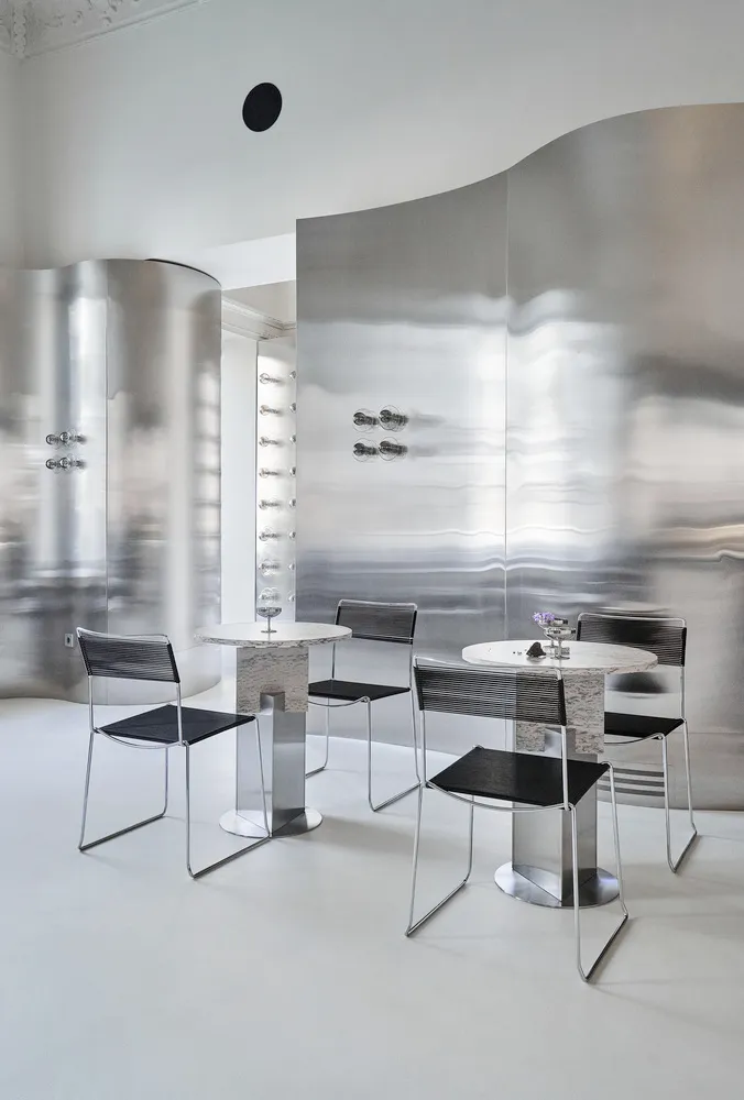 Modern dining space with two tables and chairs, silver decor, and decorative vases, under warm and inviting lighting