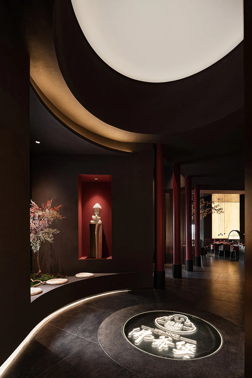 Modern restaurant dining area with multiple tables, chairs, potted plants, artwork, and red accents on the walls and ceiling