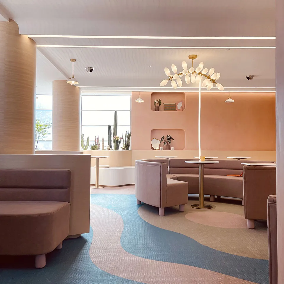 A spacious cafe with multiple couches, tables, chairs, and potted plants, creating a warm and inviting atmosphere for socializing and dining