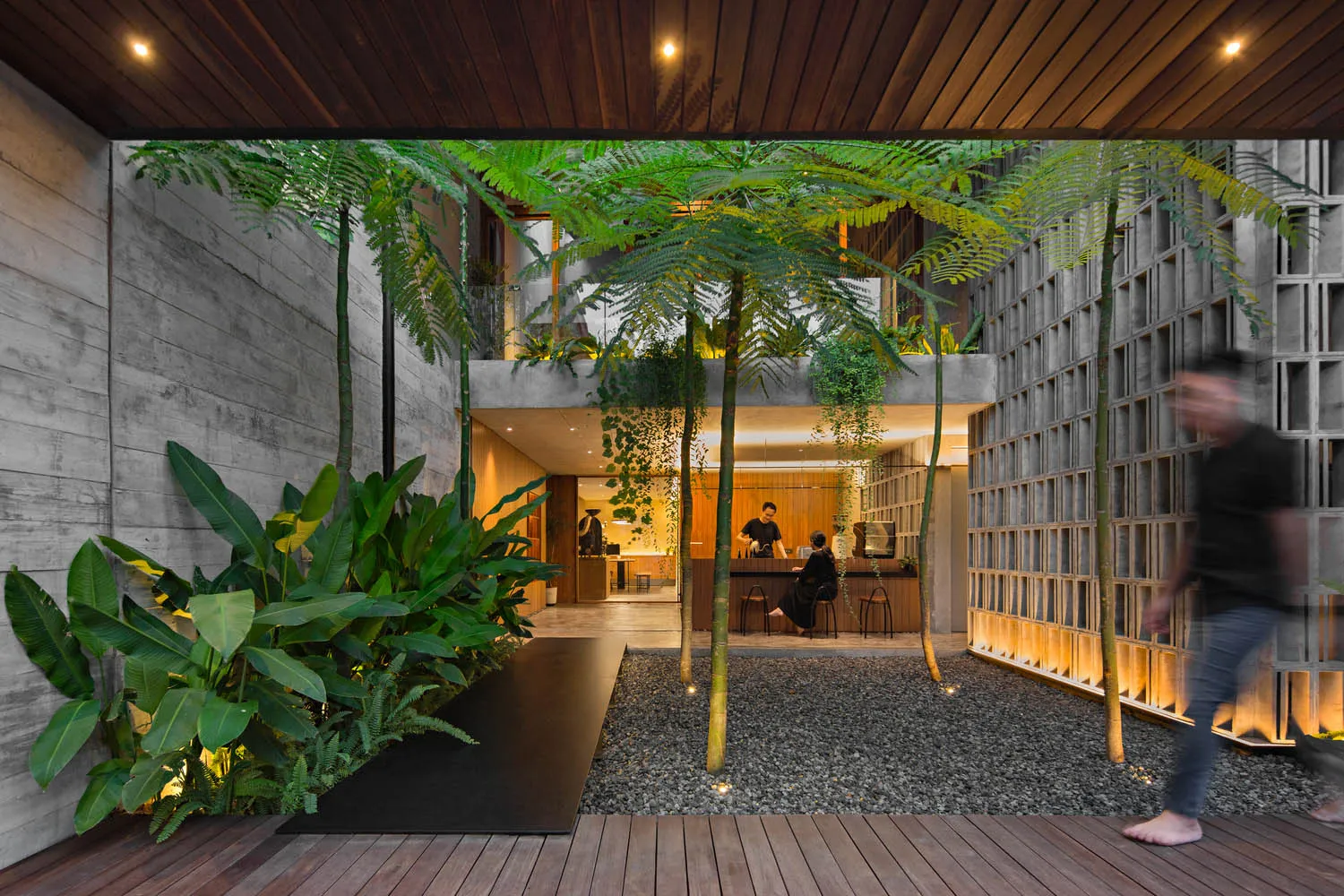 A modern cafe with a wooden floor, potted plants, and chairs arranged around dining tables, with people present in the scene