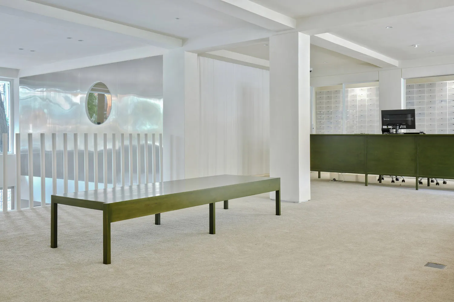 Open modern living space with white walls and flooring, featuring two tables, chairs, and a mirror, with natural light and a green tabletop