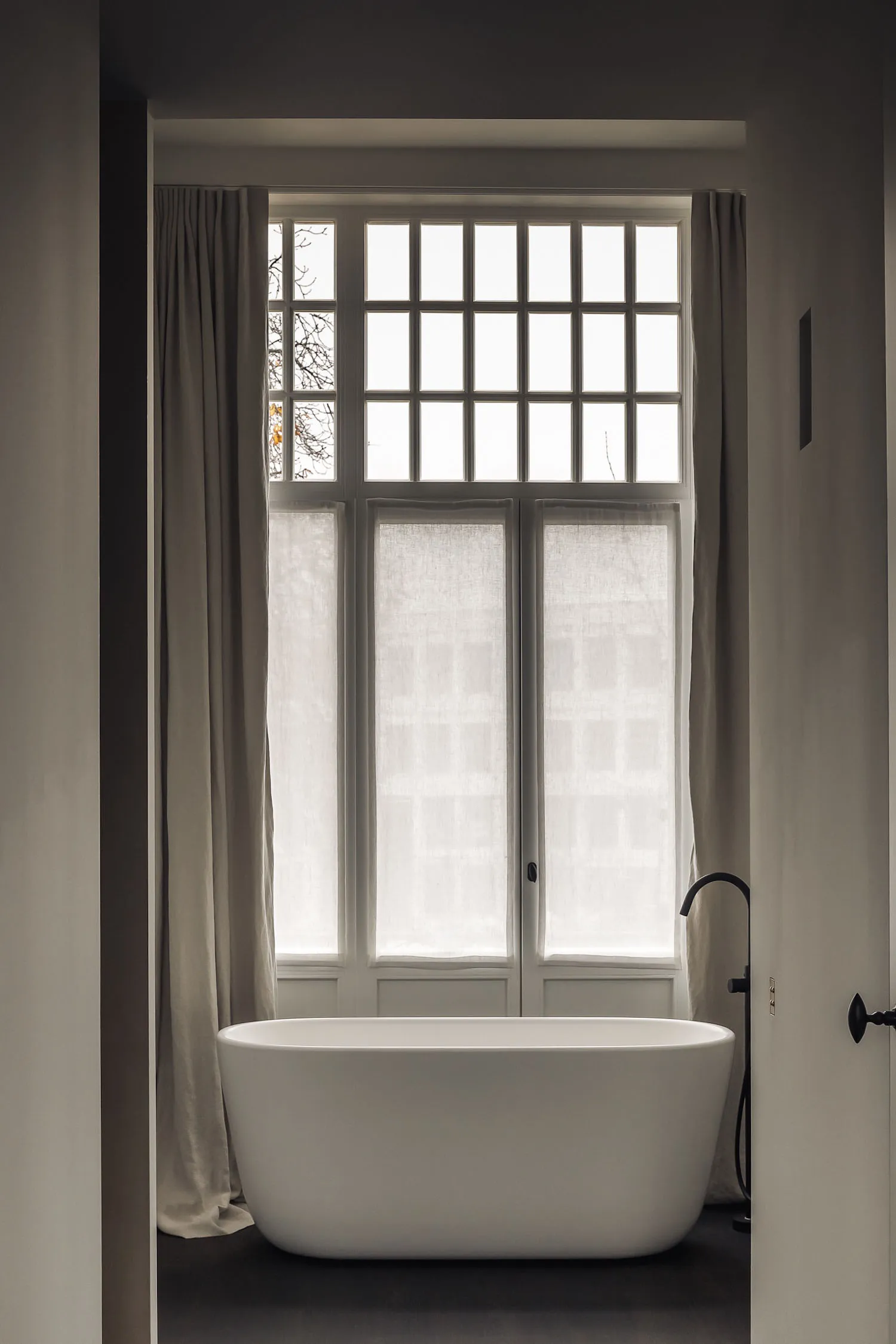 A calm bathroom with a white bathtub next to a window covered in curtains