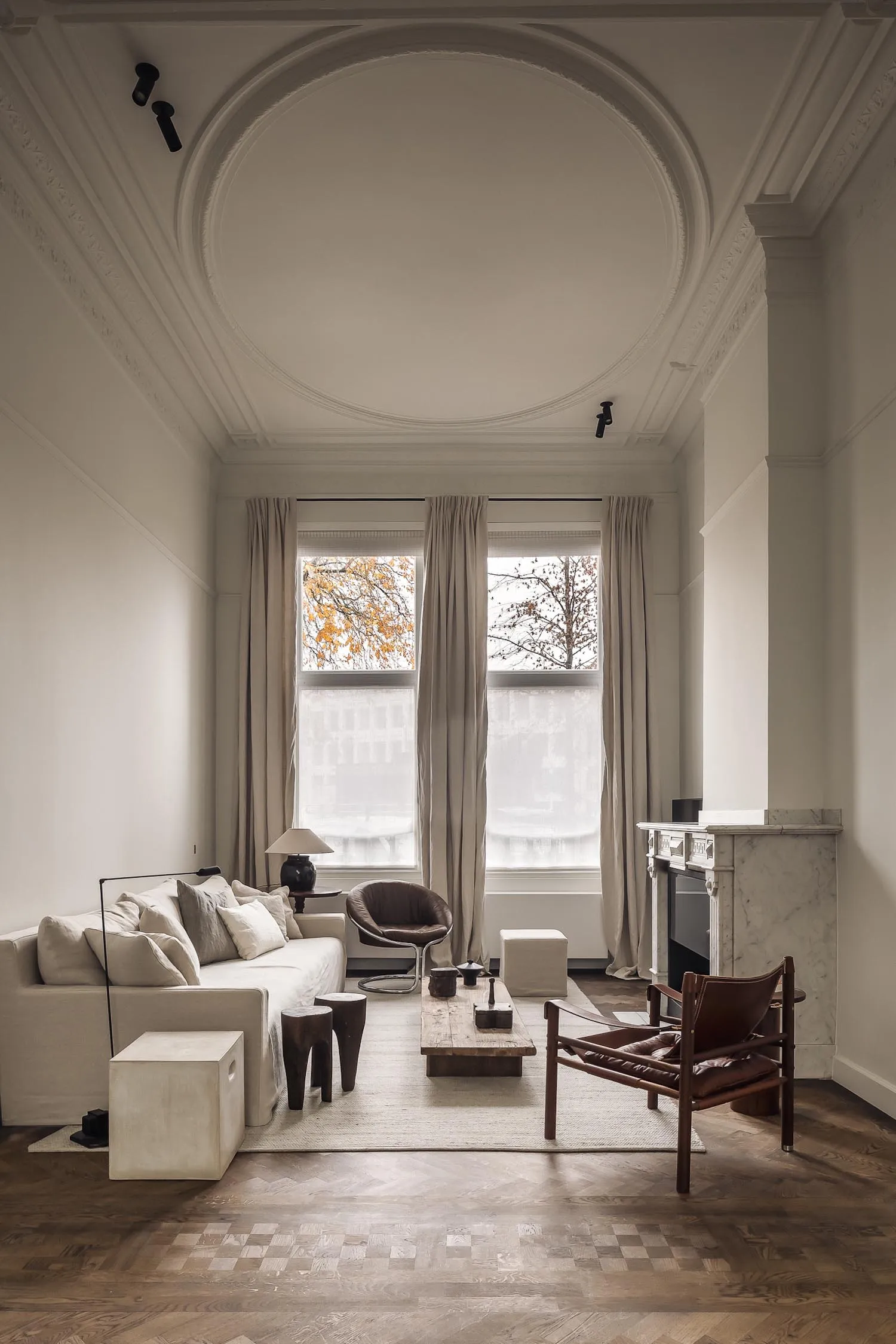 Modern living room with a white interior, wood furniture, and a fireplace, featuring two windows and a clean, bright atmosphere