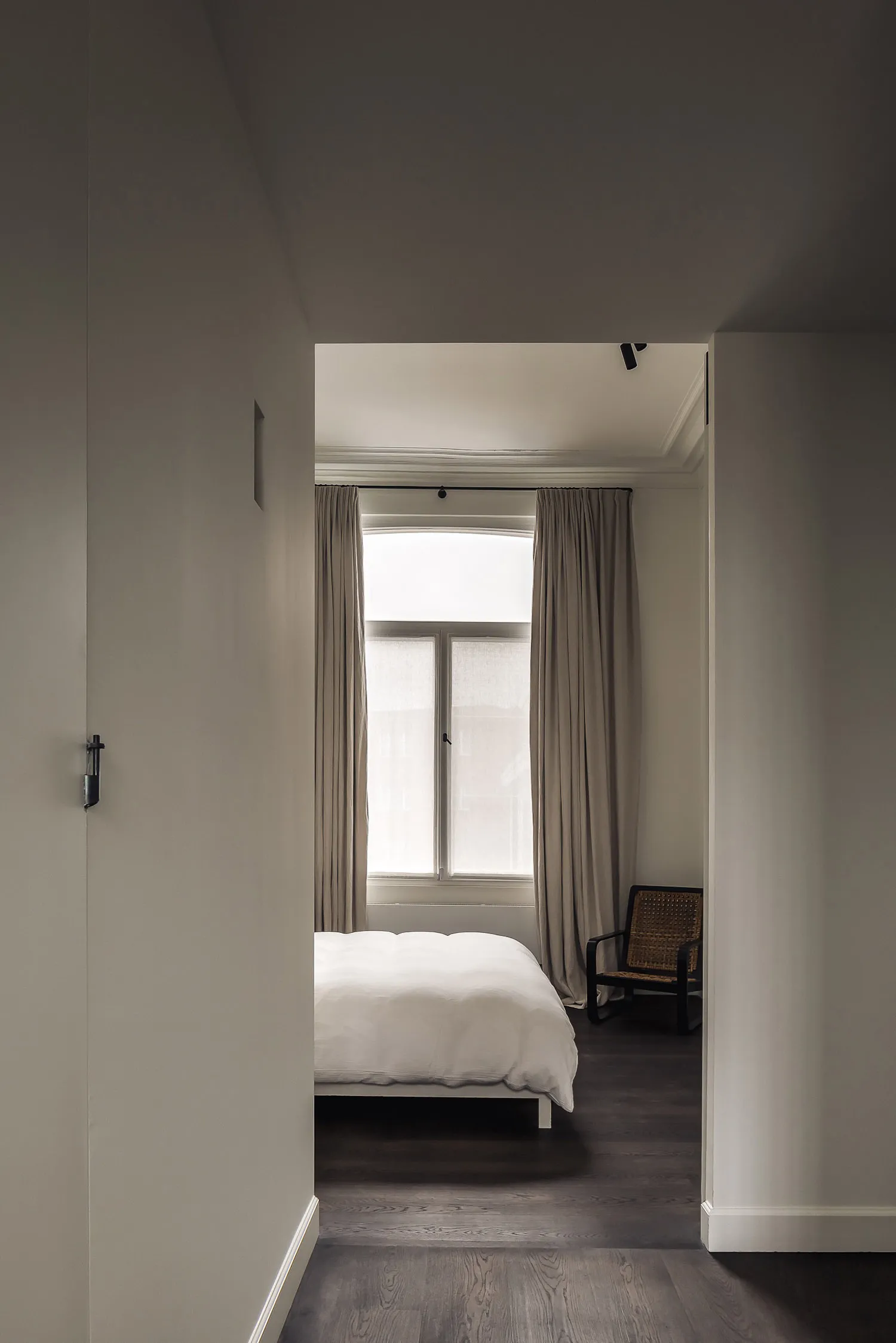A calm bedroom with a white bed in front of a large window, two chairs, and a couch, with a focus on simplicity and functionality