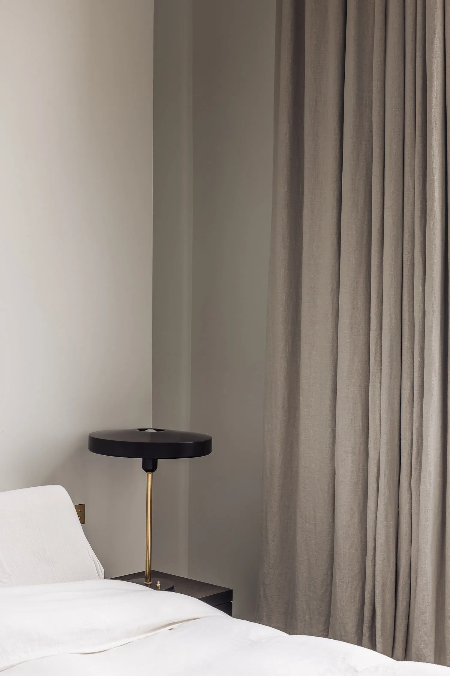 A cozy bedroom with a white bed, a black and gold lamp on each side, and a chair near the foot of the bed