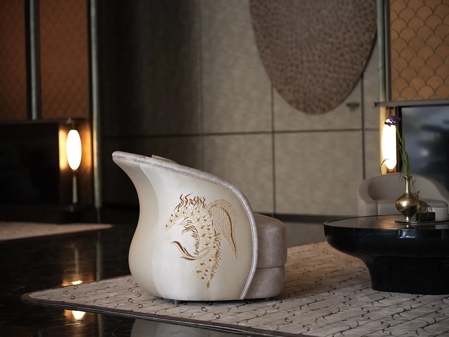 A well-lit living room with a white chair featuring gold accents and a dragon design, in front of a table, with a vase suggesting decorative elements