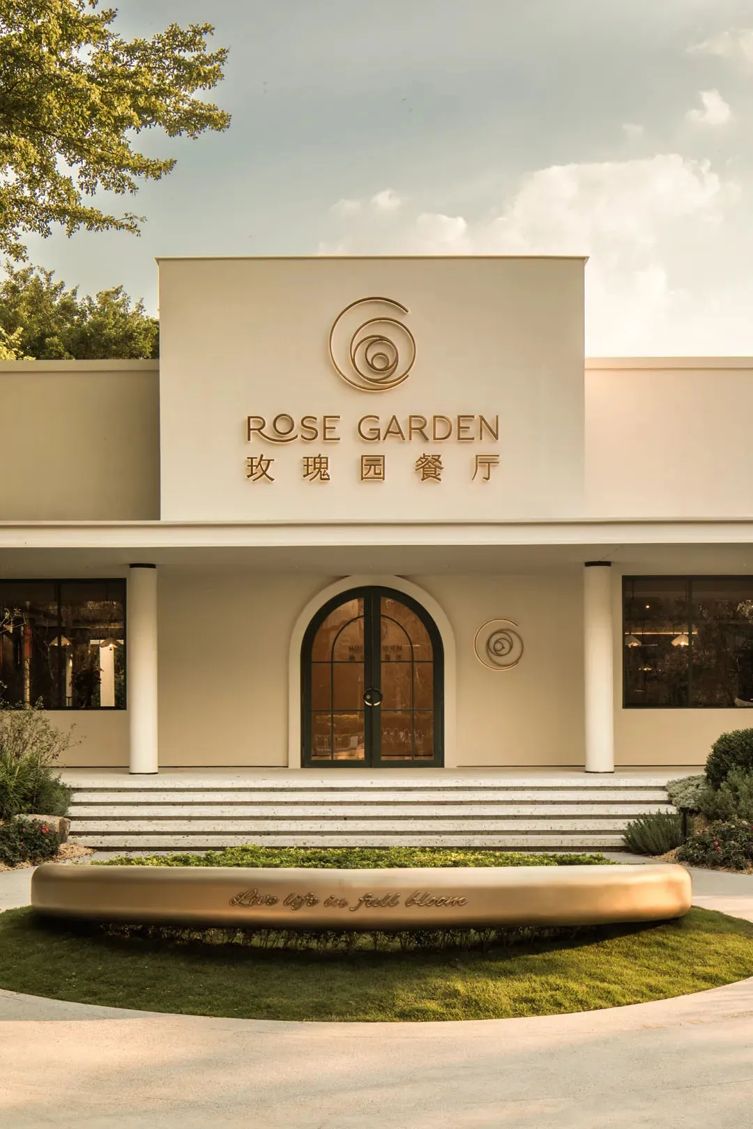 A white concrete building with a large circular window on its facade and two smaller round windows in front, possibly a garden center or similar establishment