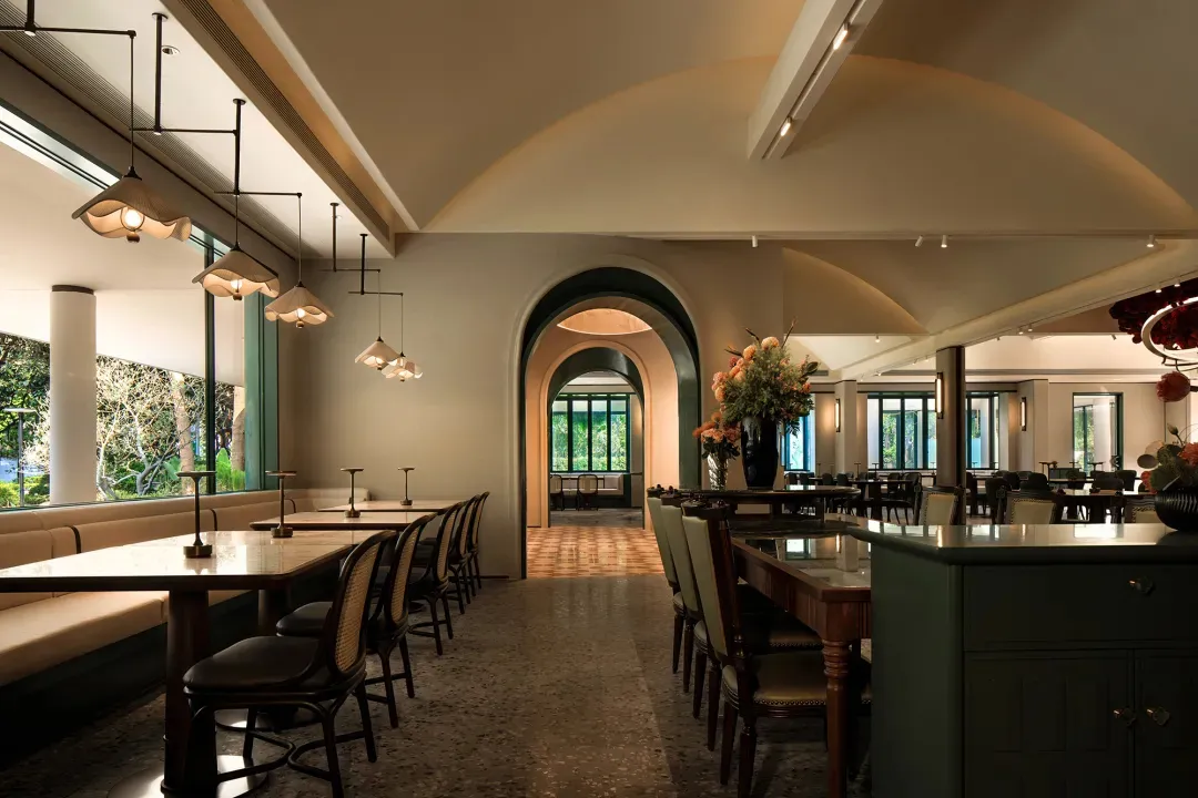 An inviting restaurant interior with a large dining table, multiple chairs, and several potted plants