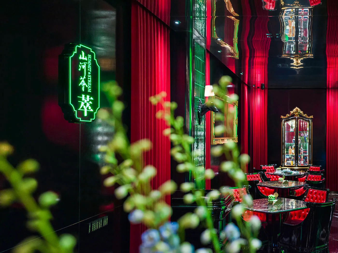 Warm and inviting Asian restaurant interior with red walls, green neon lights, chairs, tables, and a bar area with a countertop and decorative items