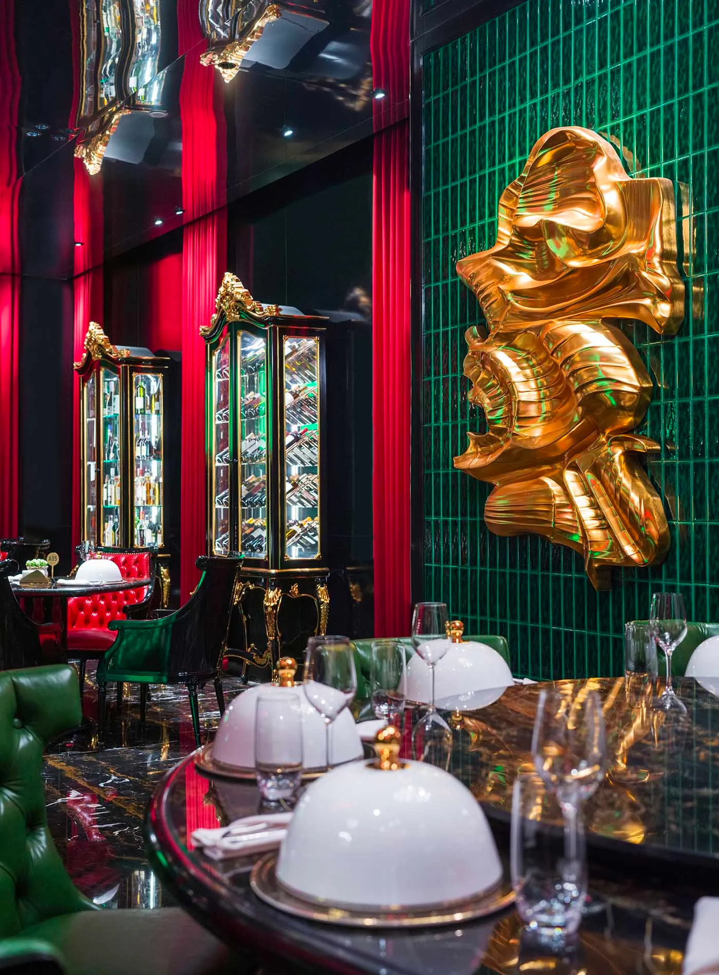 Luxurious dining area with a gold statue centerpiece, red leather chairs, and wine glasses on a table surrounded by books