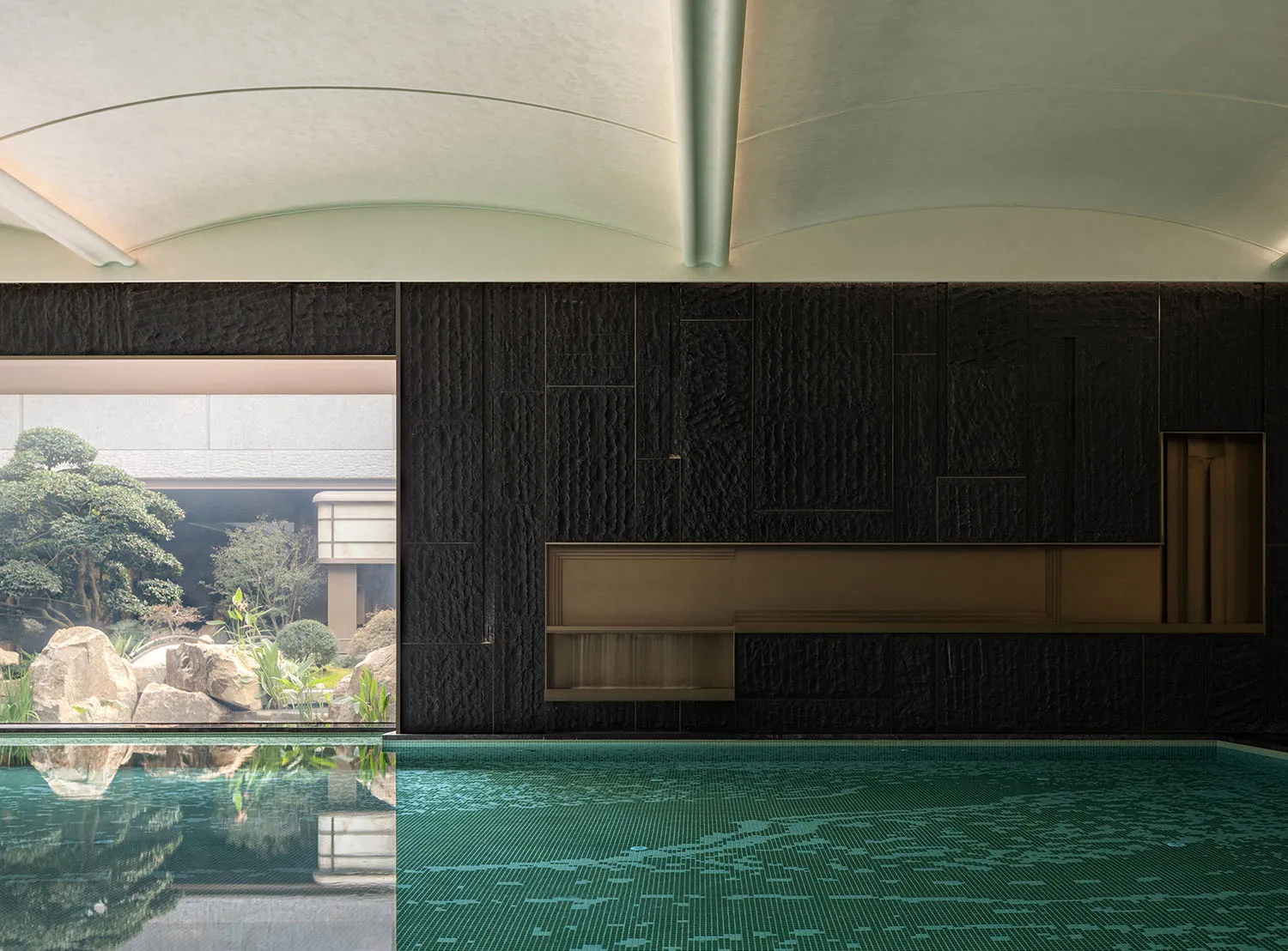 Indoor pool area with black walls, empty pool, and a bench, suggesting a luxurious and relaxing environment