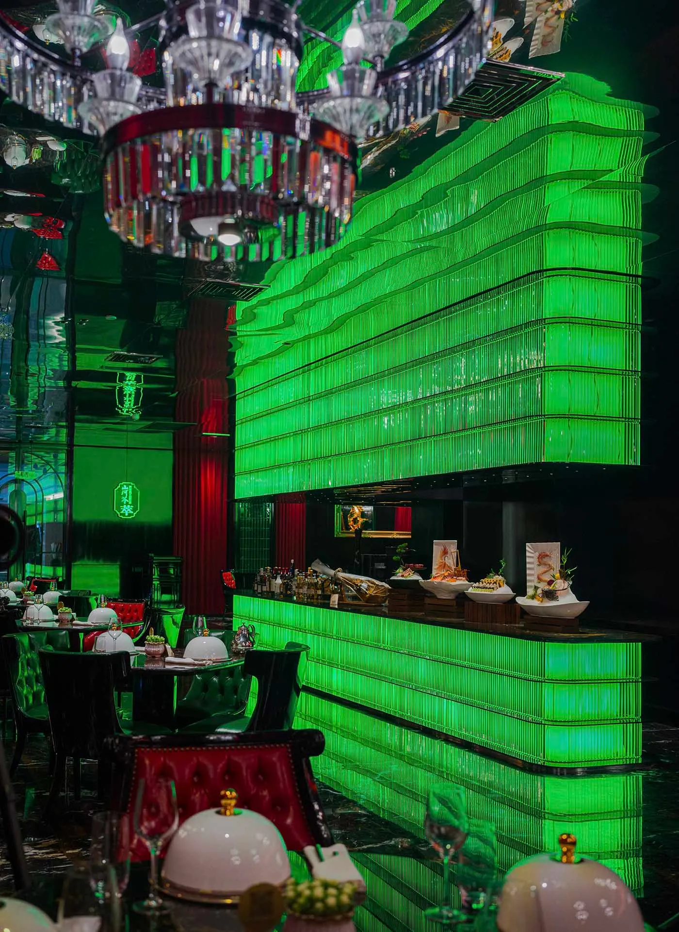 現代餐廳內部，綠色牆面、吧台區，以及鋪白桌布的餐桌與各式碗盤，背景為廚房