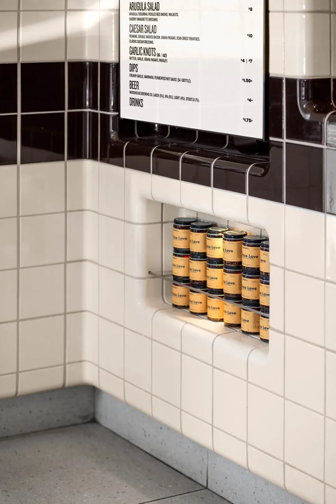 A well-organized kitchen area with a white tiled wall, lined jars, and bottles, creating a clean and commercial atmosphere