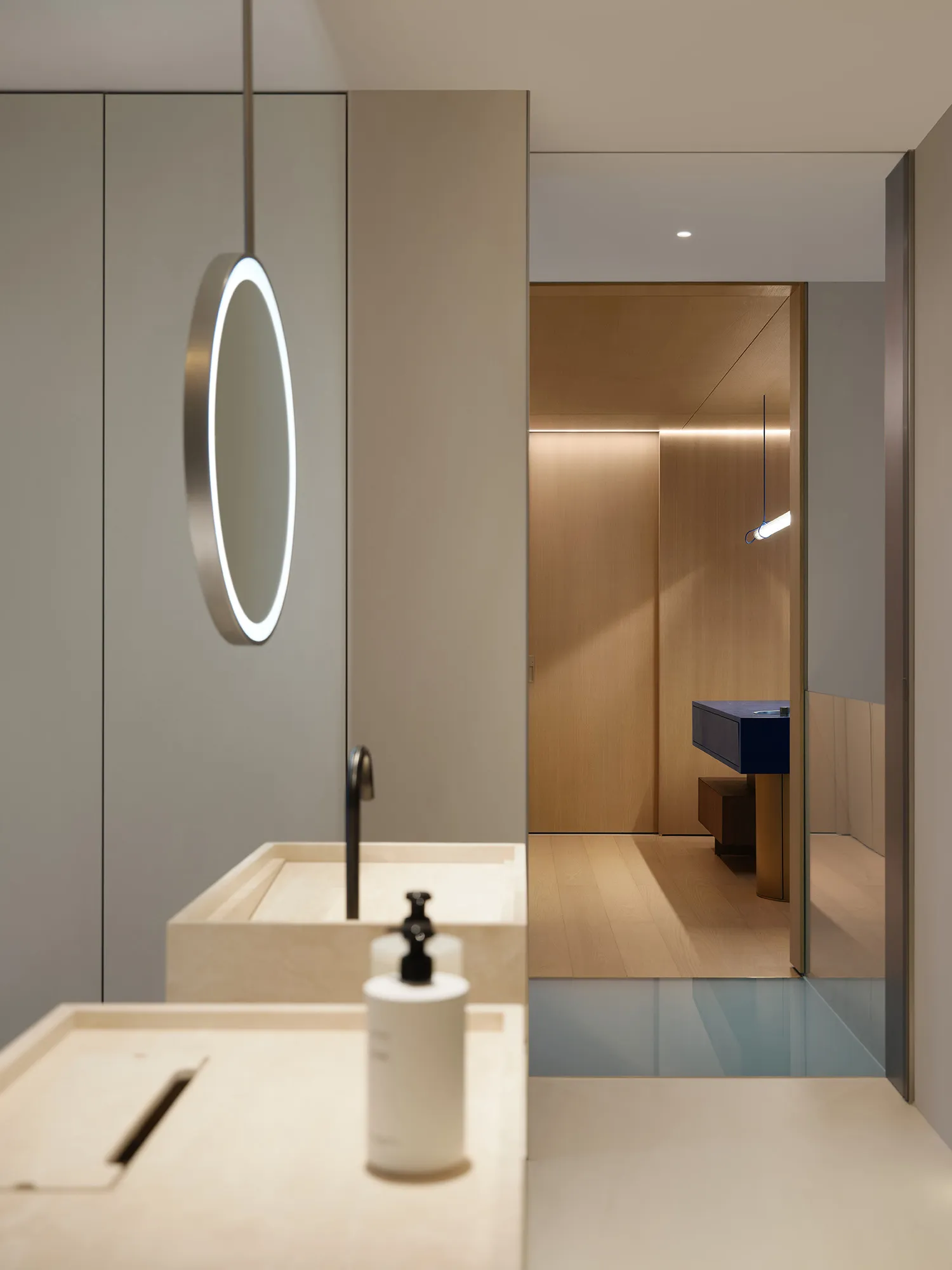 Bathroom with two sinks, a wooden floor, and a circular-framed mirror in a well-lit space
