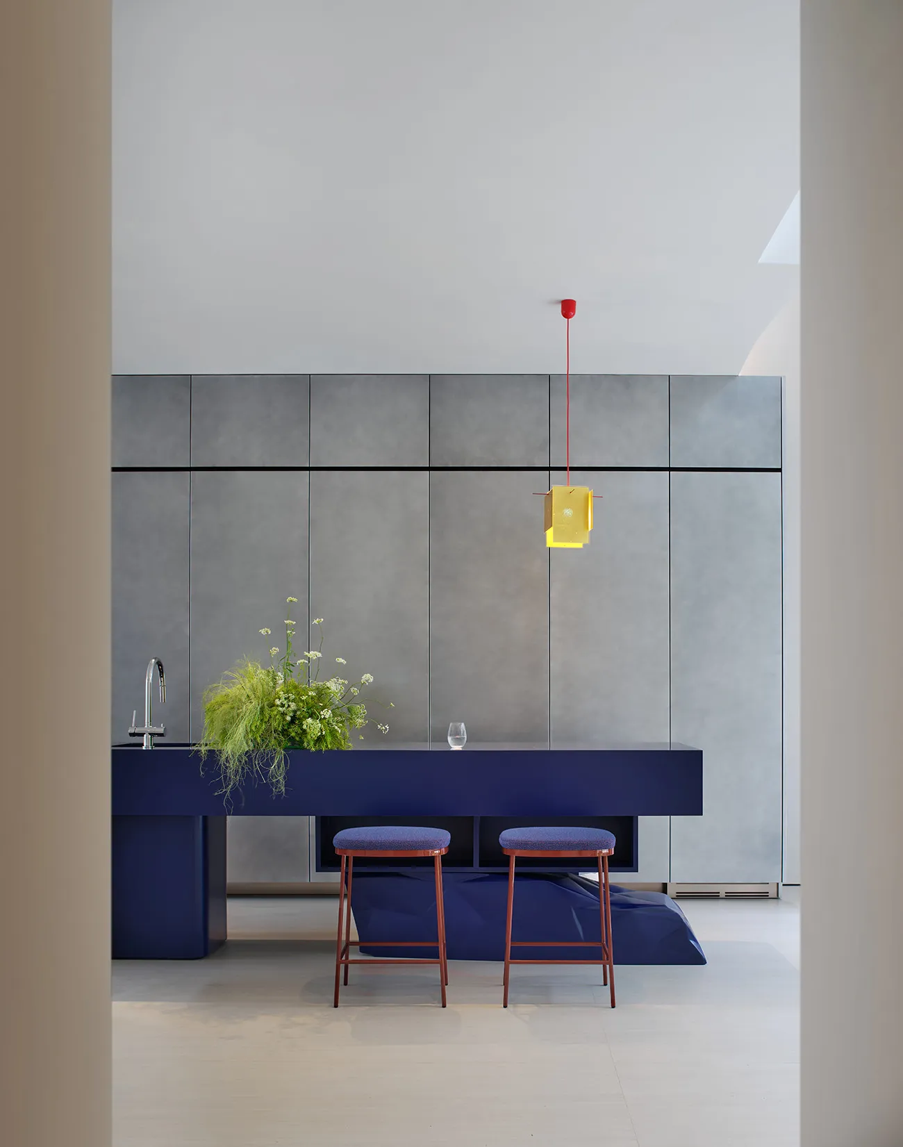 Modern kitchen with a blue countertop, grey walls, a sink, stools, and a potted plant