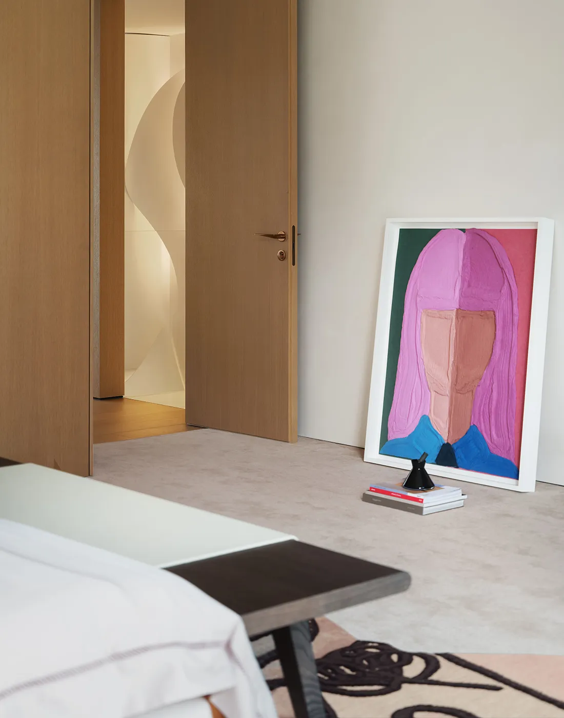 A cozy bedroom with a bed, artwork, and a wooden floor, lit by natural light and soft shadows