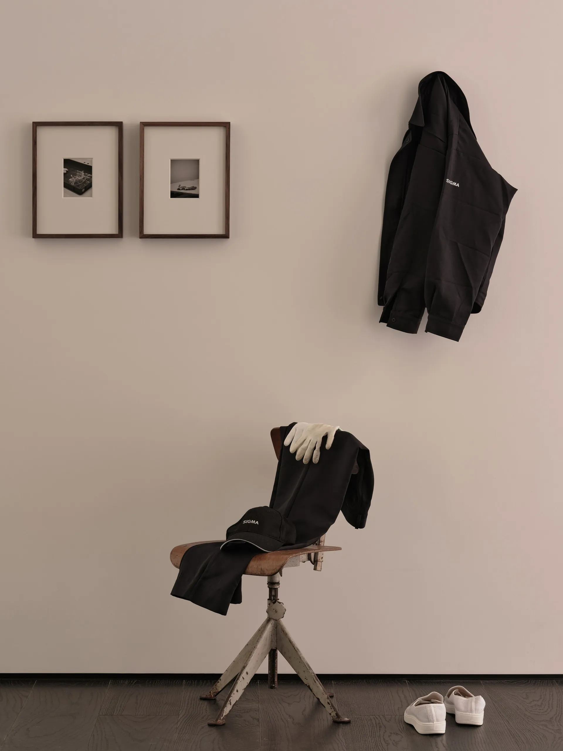 A home office with a white wall featuring two framed pictures and a chair with two black jackets and a handbag